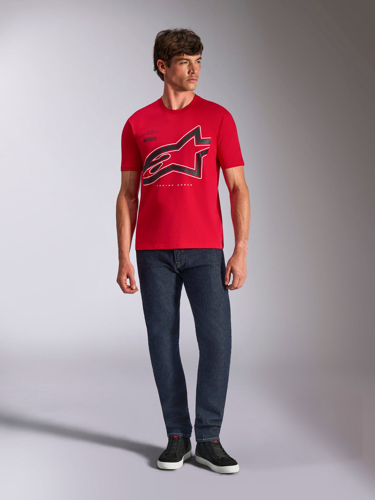 Alpinestars Authority CSF Tee, T-shirt de manga curta, vermelha, logótipo Astars grande recortado em preto com contorno branco, usada com calças de ganga azul-escuro e sapatilhas pretas, streetwear casual inspirado no desporto motorizado