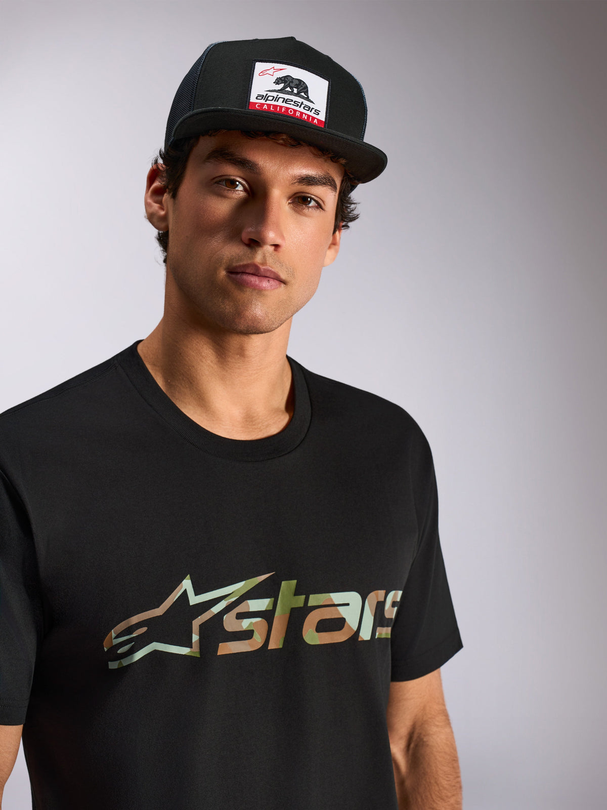 Alpinestars Verdure Camo CSF Tee, t-shirt de manga curta, preta, logótipo Astars com enchimento camuflado, usada por modelo masculino com boné trucker Alpinestars California preto, streetwear casual de desporto motorizado