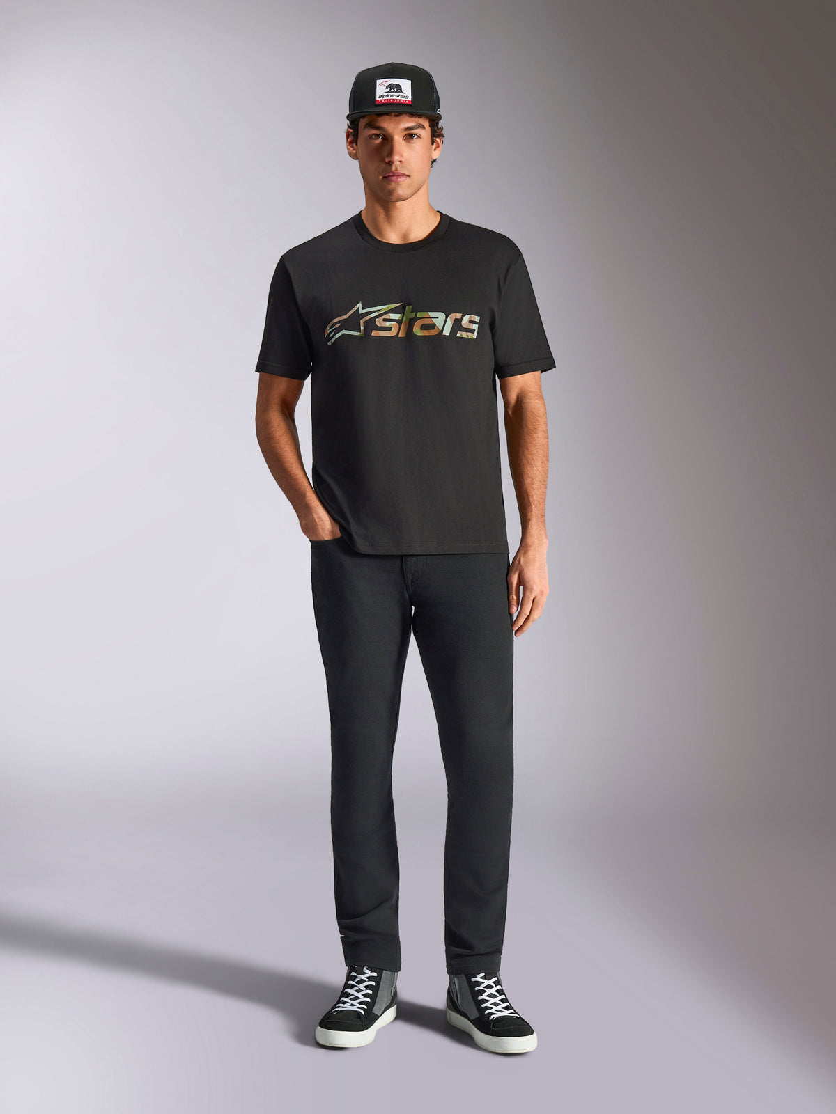 Alpinestars Verdure Camo CSF Tee, t-shirt de manga curta, preta, com o logótipo Astars em padrão camuflado no peito, usada por um modelo com boné preto e calças pretas, streetwear casual de desportos motorizados
