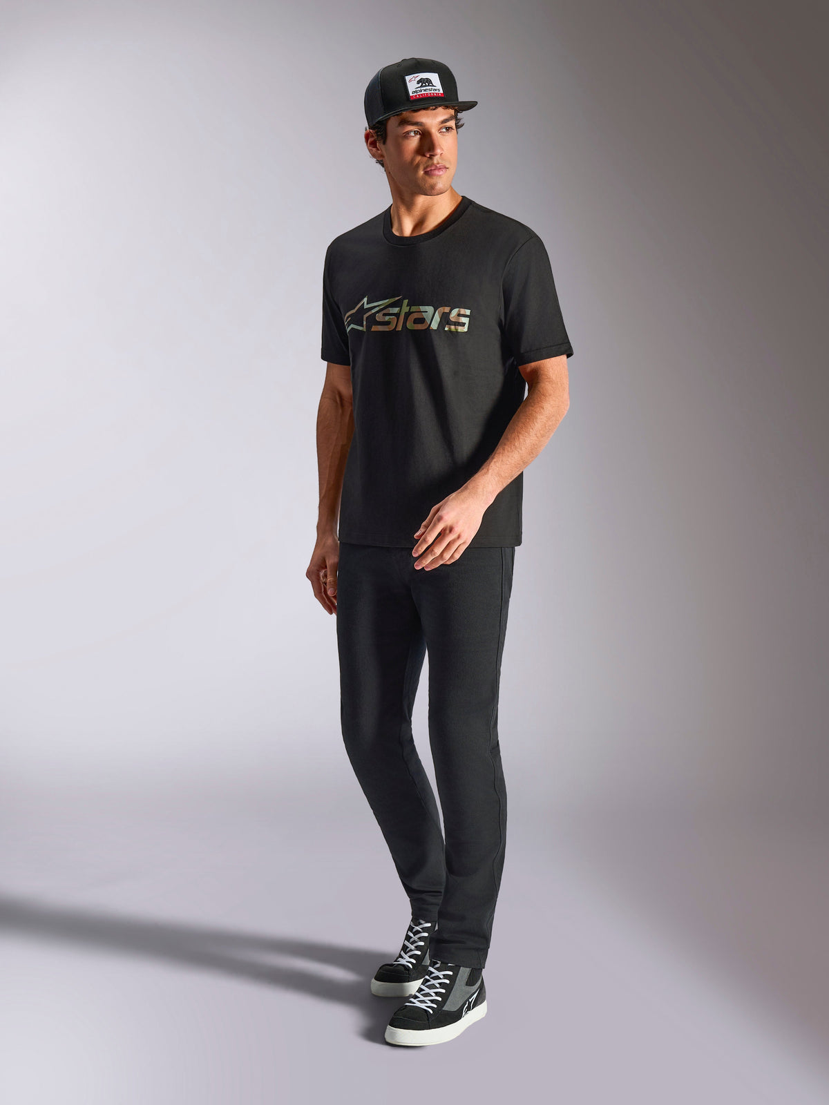 Alpinestars Verdure Camo CSF Tee, t-shirt de manga curta, preta, com logótipo Astars com enchimento camuflado no peito, usada por um modelo com boné e calças pretas, streetwear casual de motorsport