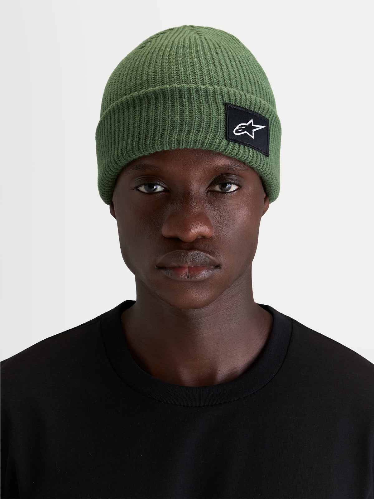 Gorro Alpinestars Unload Rib Cuff, gorro de malha verde, vista frontal num modelo a mostrar a silhueta de ajuste raso e o patch tecido SAstars