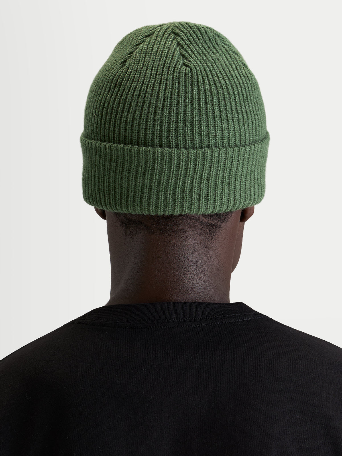 Alpinestars Gorro Unload Rib Cuff, gorro de inverno sportswear em malha, verde-ervilha, vista traseira num modelo a usar uma t-shirt preta, mostrando a construção em ponto jersey acrílico e o ajuste clássico raso