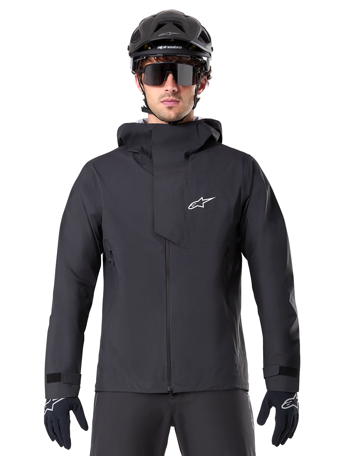 Alpinestars A-Dura Elite Waterproof Jacket, casaco de BTT impermeável, preto, gola alta com capuz, fecho frontal com aba protetora no peito e logótipo branco, usado com capacete e luvas de ciclismo pretos, proteção técnica para trilhos