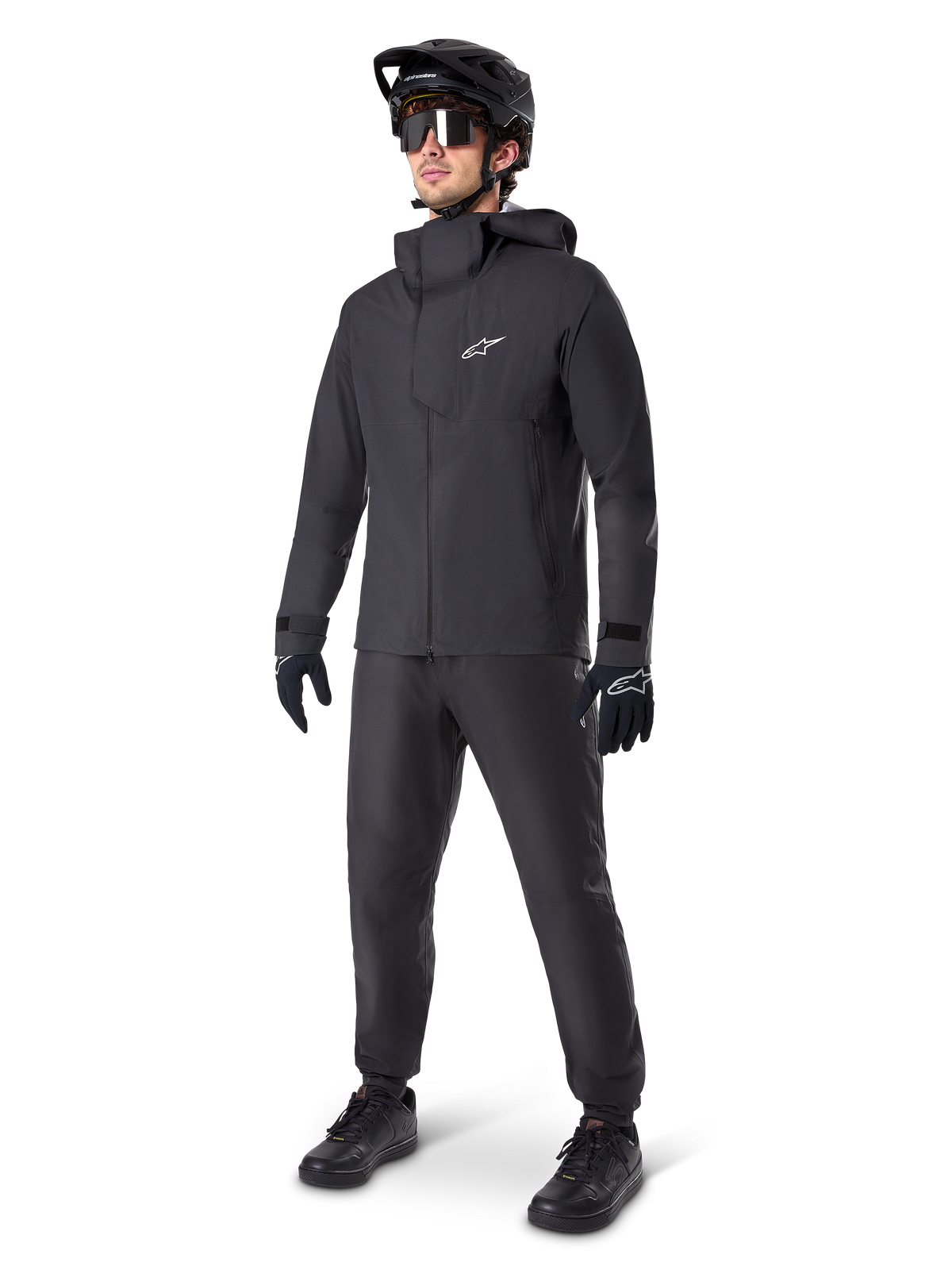 Casaco impermeável Alpinestars A-Dura Elite em preto, usado por um ciclista masculino com calças de BTT, luvas e capacete pretos a condizer. O casaco apresenta um design técnico impermeável com um logótipo Astars branco no peito e uma gola alta protetora.
