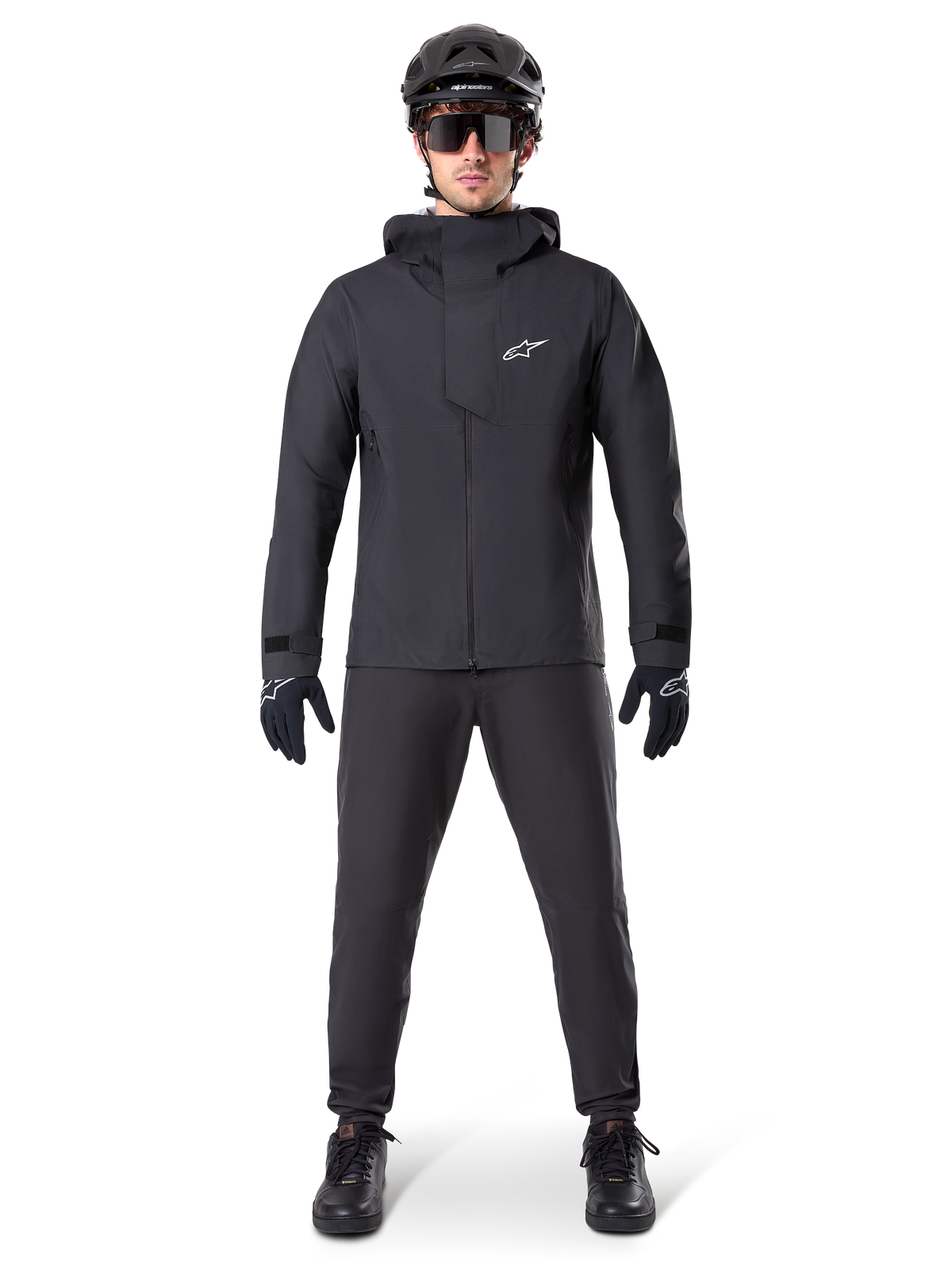 Casaco Impermeável Alpinestars A-Dura Elite, preto, usado com calças de ciclismo e luvas a condizer, capacete preto e óculos de sol, com um logótipo Astars branco no peito, design técnico de alto desempenho para BTT