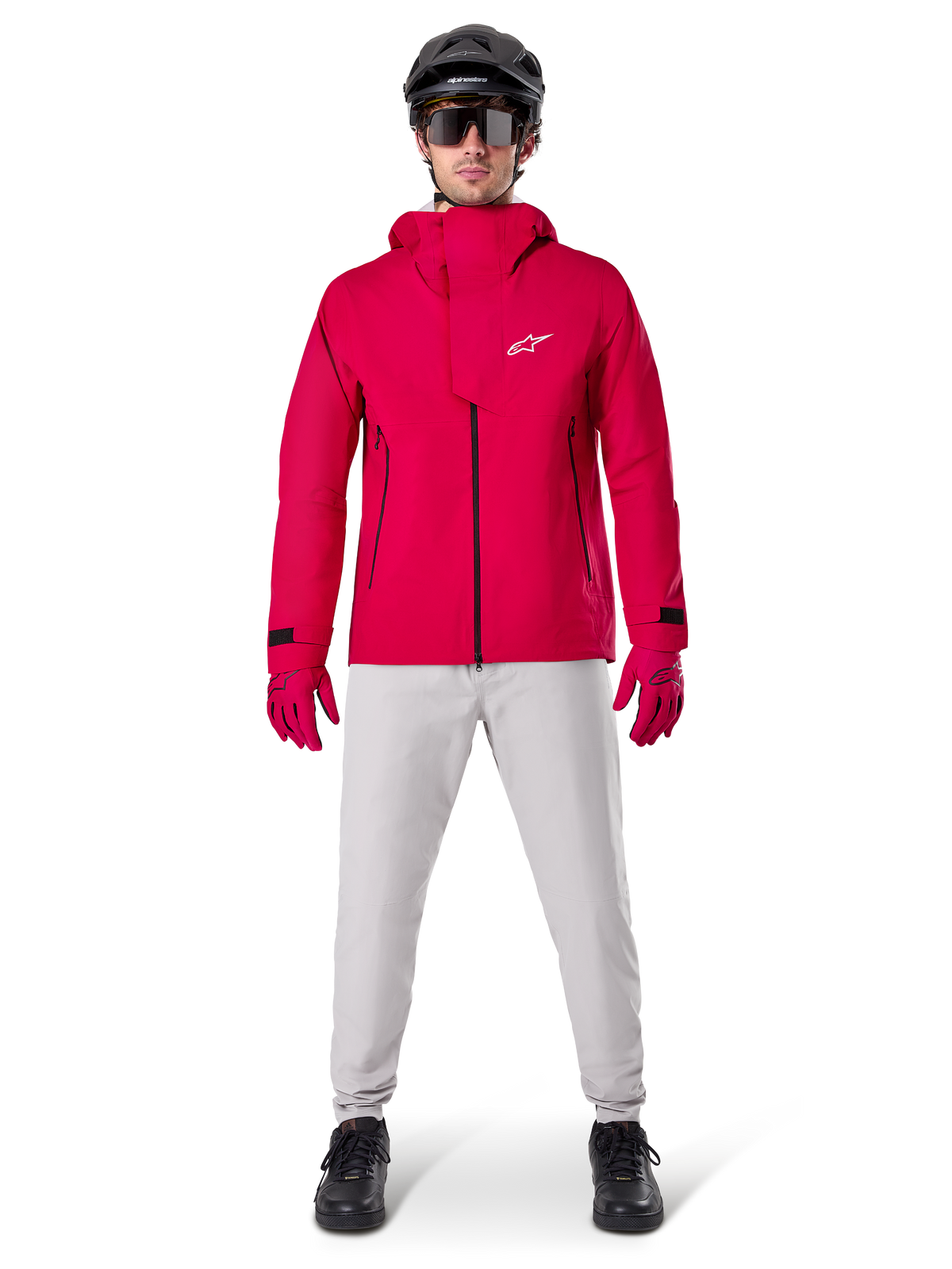 Casaco Impermeável Alpinestars A-Dura Elite, Vermelho Fluo, casaco técnico de BTT usado com um capacete de BTT preto, óculos de sol, luvas vermelhas a condizer e calças cinzentas claras, vista de corpo inteiro de equipamento de ciclismo para todas as condições meteorológicas