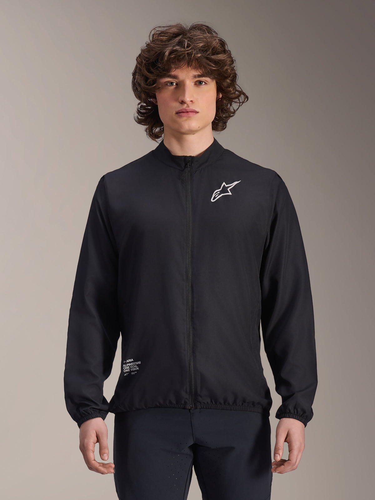 Casaco Corta-Vento Alpinestars A-Aria, preto, casaco de ciclismo leve, com logótipo Astars branco no peito e marca na parte inferior direita, fecho de correr frontal integral, gola subida, punhos e bainha elásticos, ajuste de performance para desportos ao ar livre