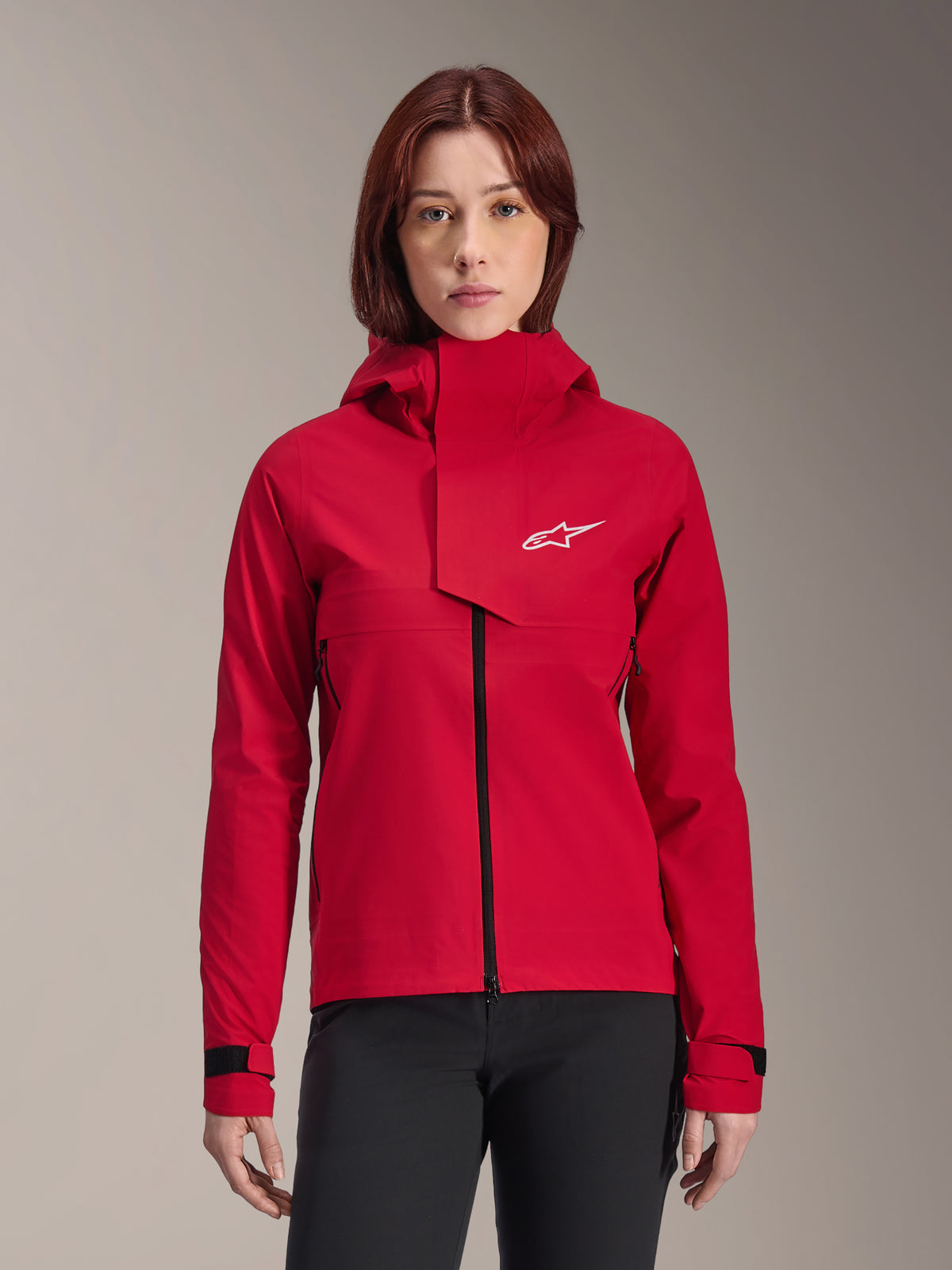 Alpinestars Stella A-Dura Elite Waterproof Jacket, casaco de BTT para mulher, vermelho fluo, design com capuz e aba frontal assimétrica, logótipo Alpinestars branco no peito, punhos pretos ajustáveis, vestido por uma modelo com calças pretas
