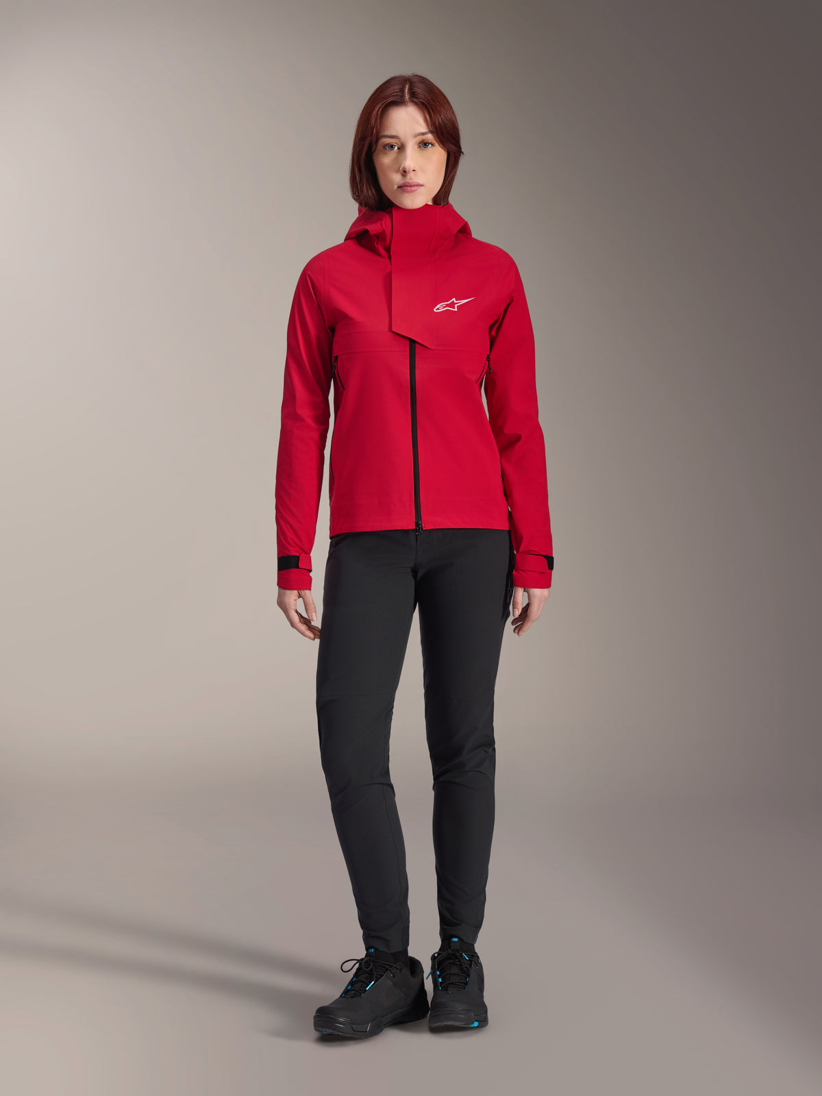 Casaco Impermeável Alpinestars Stella A-Dura Elite, casaco de BTT para mulher, Vermelho Fluo, usado com calças e sapatos pretos, com capuz de gola alta e logótipo Alpinestars branco, vestuário técnico de mountain bike