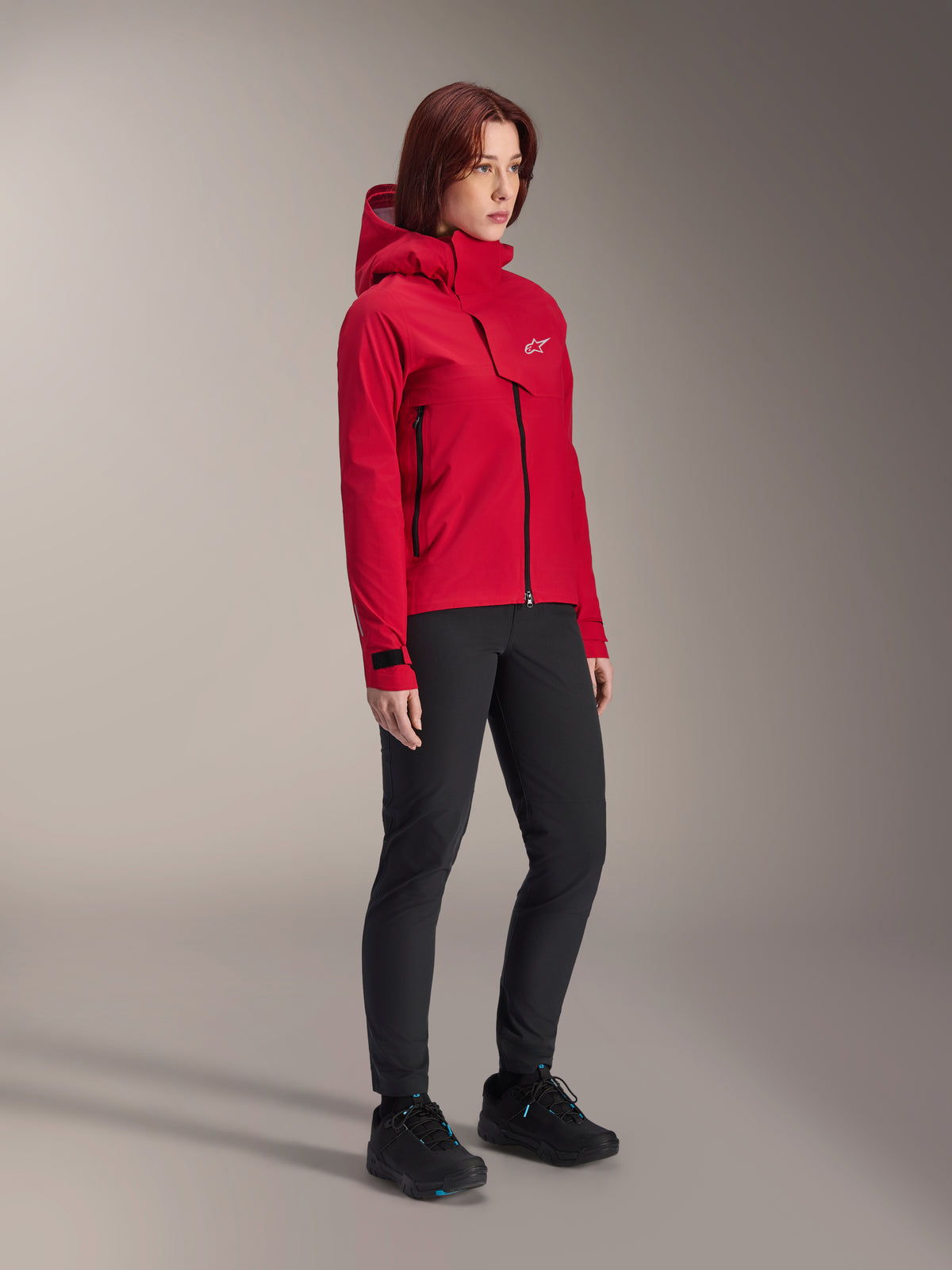 Alpinestars Stella A-Dura Elite Waterproof Jacket para mulher, Vermelho Fluo, casaco impermeável com capuz para BTT com logótipo Astars branco na aba do peito, usado com calças pretas e sapatilhas de BTT pretas, equipamento técnico de alto desempenho para trilhos