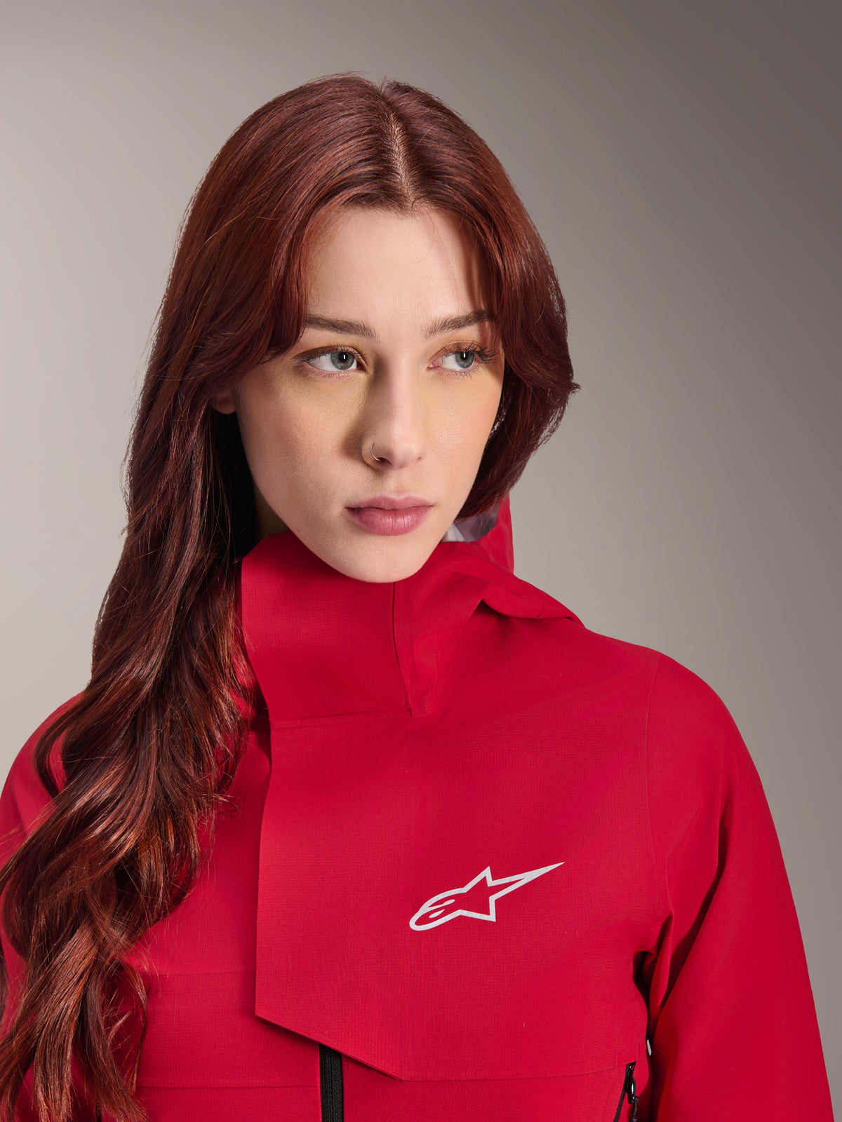 Casaco Impermeável Alpinestars Stella A-Dura Elite, Vermelho Fluo, usado por uma mulher com cabelo ruivo comprido, casaco técnico impermeável de 3 camadas com gola alta e logótipo branco, equipamento de alta performance para outdoor e mountain bike
