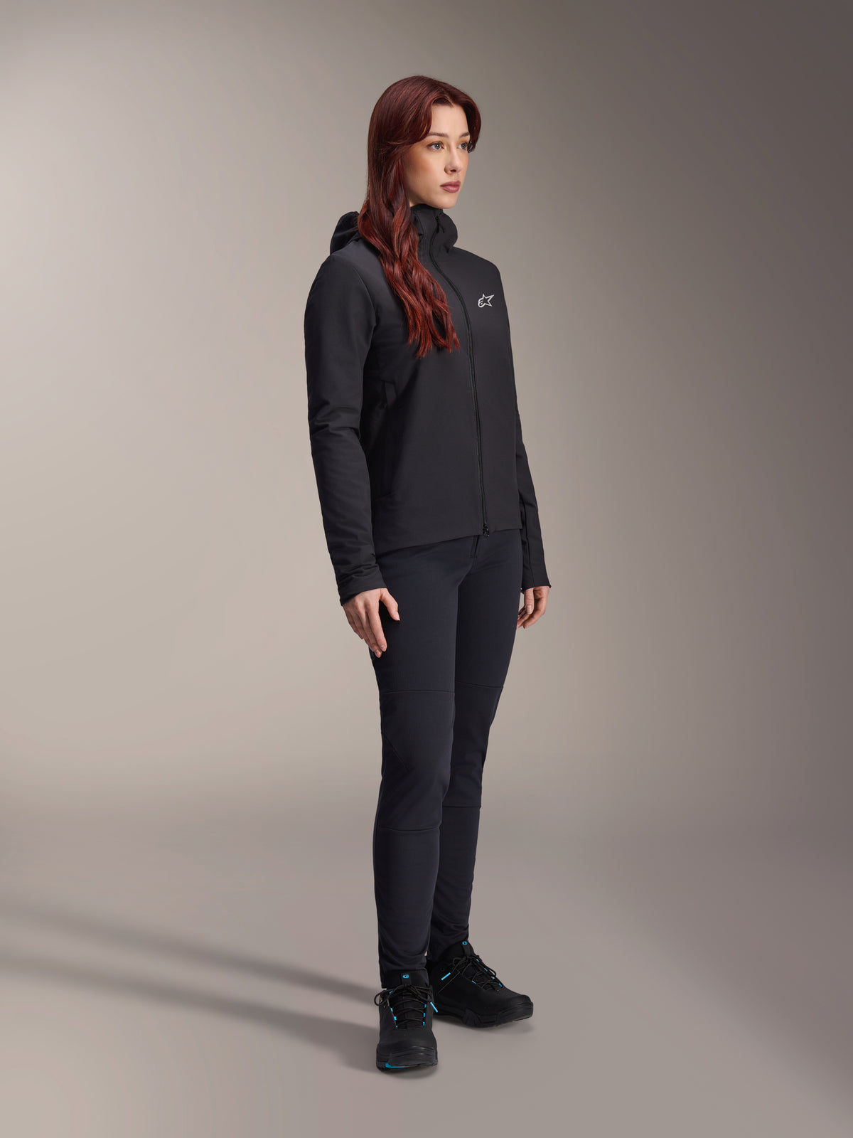 Casaco Térmico Alpinestars Stella A-Dura, casaco preto leve com isolamento térmico e capuz para mulher, usado com calças pretas e sapatos pretos, equipamento profissional de ciclismo e BTT para condições de frio
