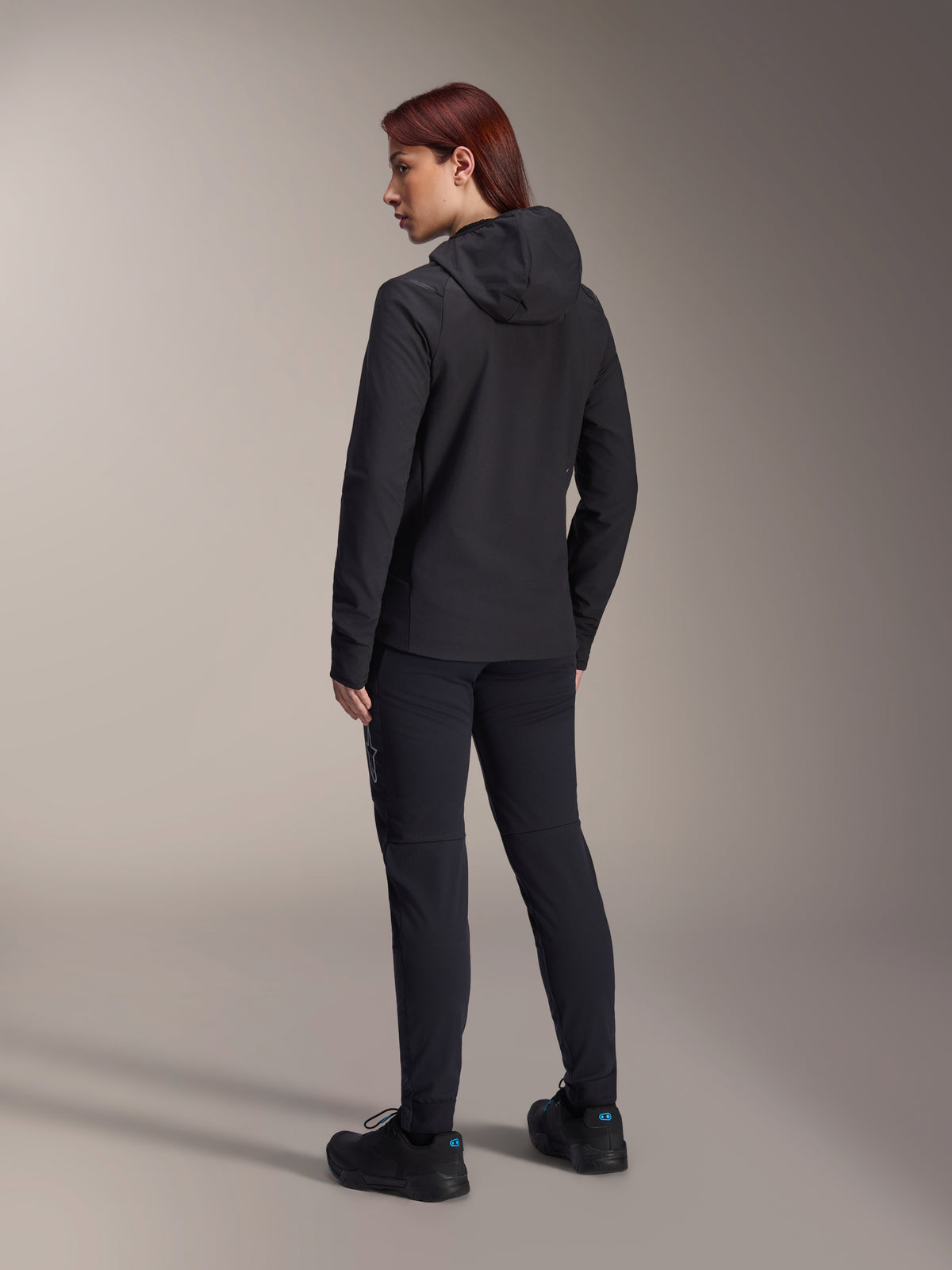 Alpinestars Stella A-Dura Thermal Jacket, casaco de ciclismo de BTT para mulher, preto, vista traseira destacando o capuz isolado e o ajuste regular, usado com calças e sapatos pretos a condizer, isolamento térmico leve para condução em tempo frio