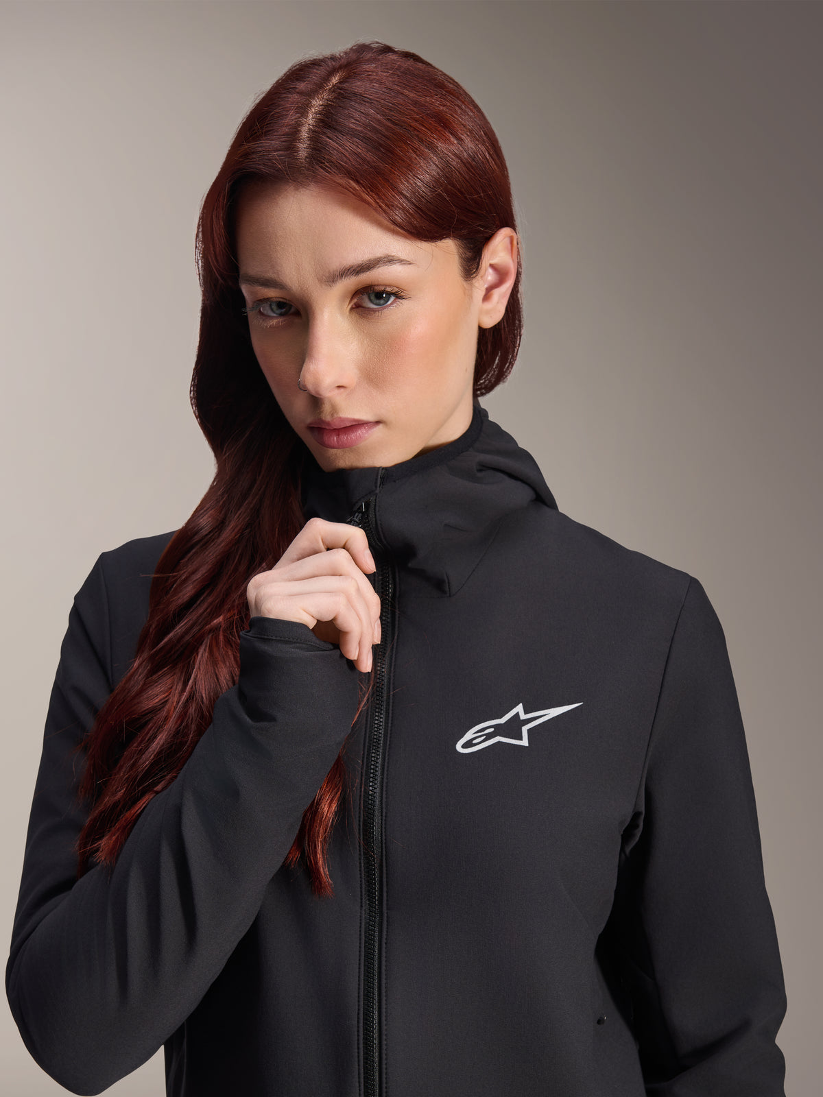 Casaco Térmico Alpinestars Stella A-Dura, casaco de ciclismo feminino preto, usado por uma modelo com cabelo comprido ruivo, logótipo Alpinestars branco no peito, design com capuz e fecho de correr frontal, vestuário de BTT