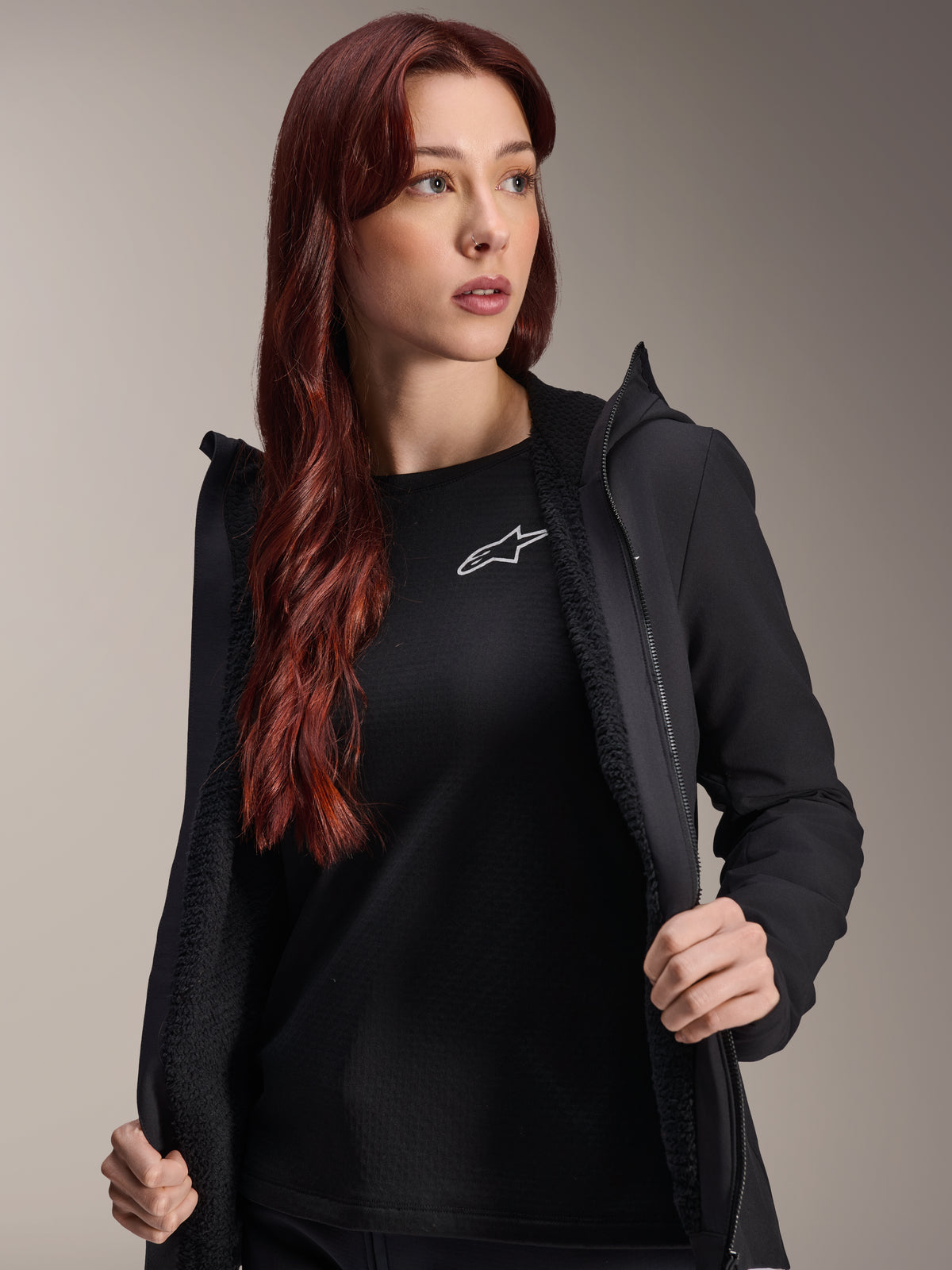 Alpinestars Stella A-Dura Thermal Jacket, casaco de ciclismo feminino preto, apresentado aberto com forro em lã texturizada e fecho frontal, usado sobre uma t-shirt preta com o logótipo da Alpinestars, leve e isolado para ciclismo em tempo frio