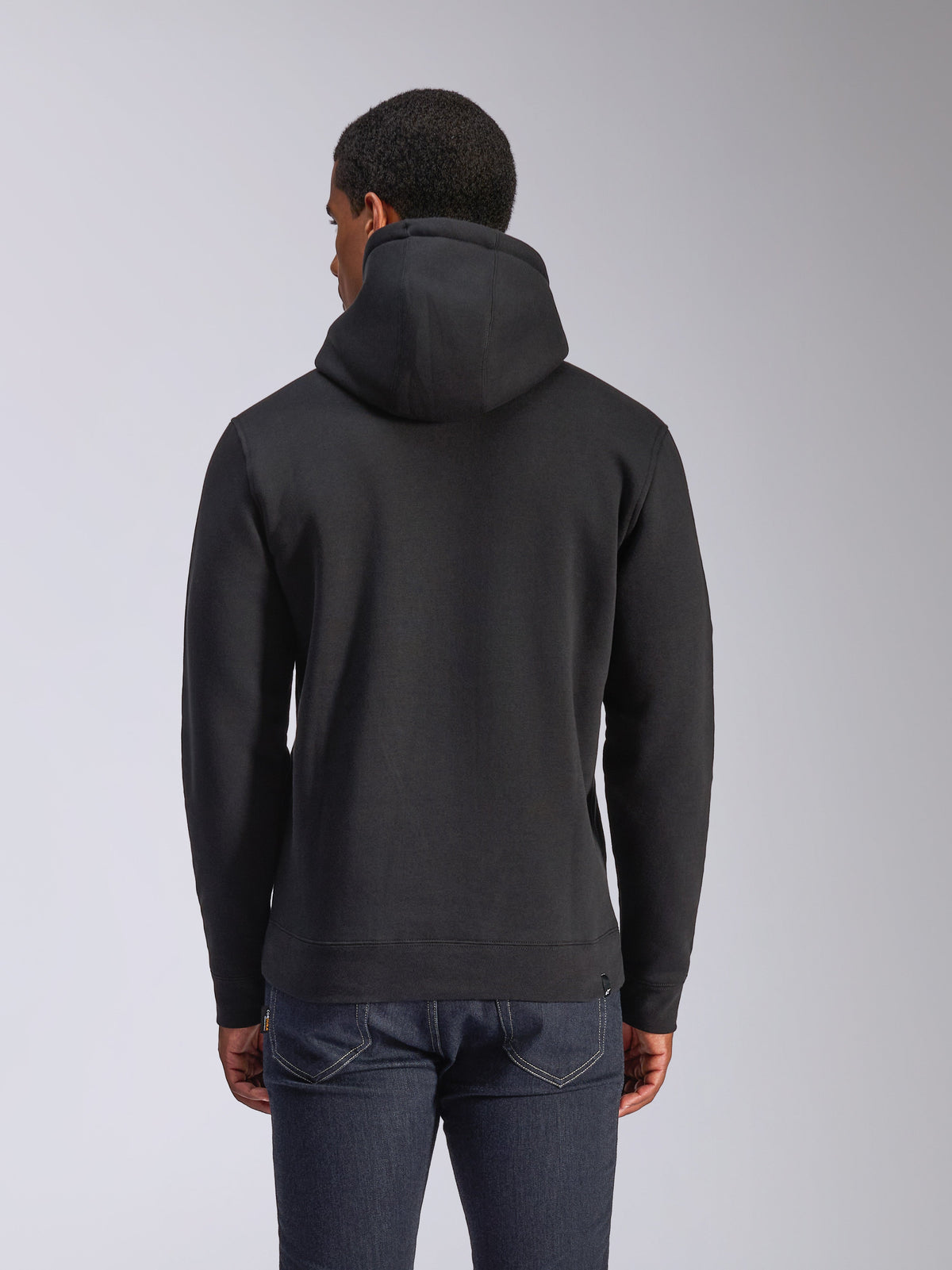 Alpinestars Blaze V3 Hoodie, vista traseira de hoodie preto em fleece, streetwear casual, com punhos e bainha canelados, capuz forrado em jersey, usado com calças de ganga azul escuro