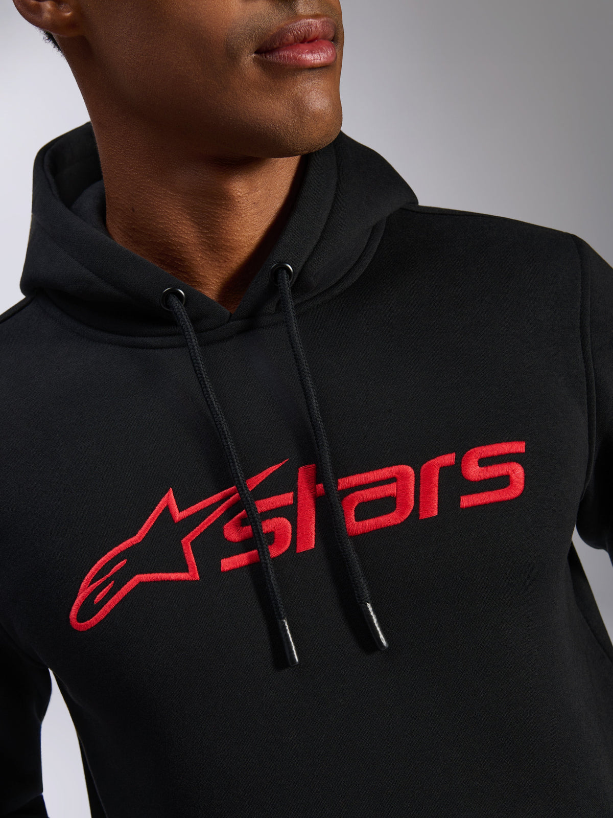 Alpinestars Blaze V3 Hoodie, vista aproximada do peito, tecido preto com logótipo Alpinestars linear estampado a vermelho, capuz com cordão e pontas mergulhadas, estilo streetwear casual inspirado no desporto motorizado
