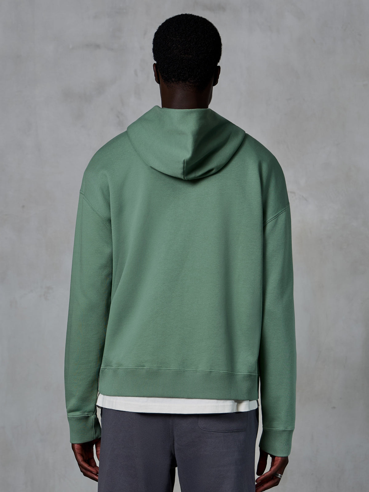 Hoodie Essentials Ageless com Fecho da Alpinestars, vista traseira num modelo, verde Cactus, streetwear casual inspirado no desporto motorizado, ajuste relaxado com bainha e punhos canelados, fleece compacto de alta qualidade