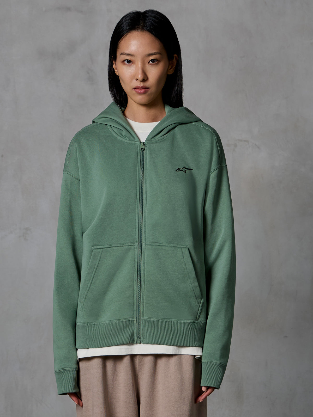 Alpinestars Essentials Ageless Zip Hoodie, verde Cactus, streetwear casual vestido por modelo feminina, hoodie de fleece com fecho, pequeno logótipo preto no peito, bolsos frontais, corte relaxado para o dia a dia