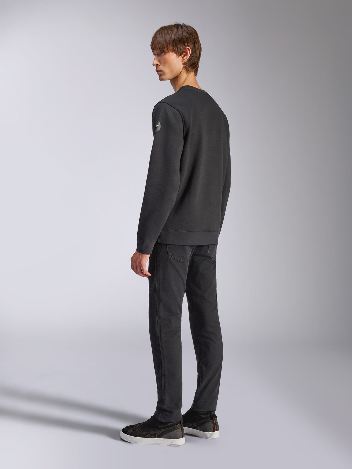 Alpinestars Bettern Crew, camisola de lã preta, modelo masculino visto de perfil e de costas, com punhos e bainha canelados e um pequeno logótipo na manga, streetwear casual de inspiração motorsport