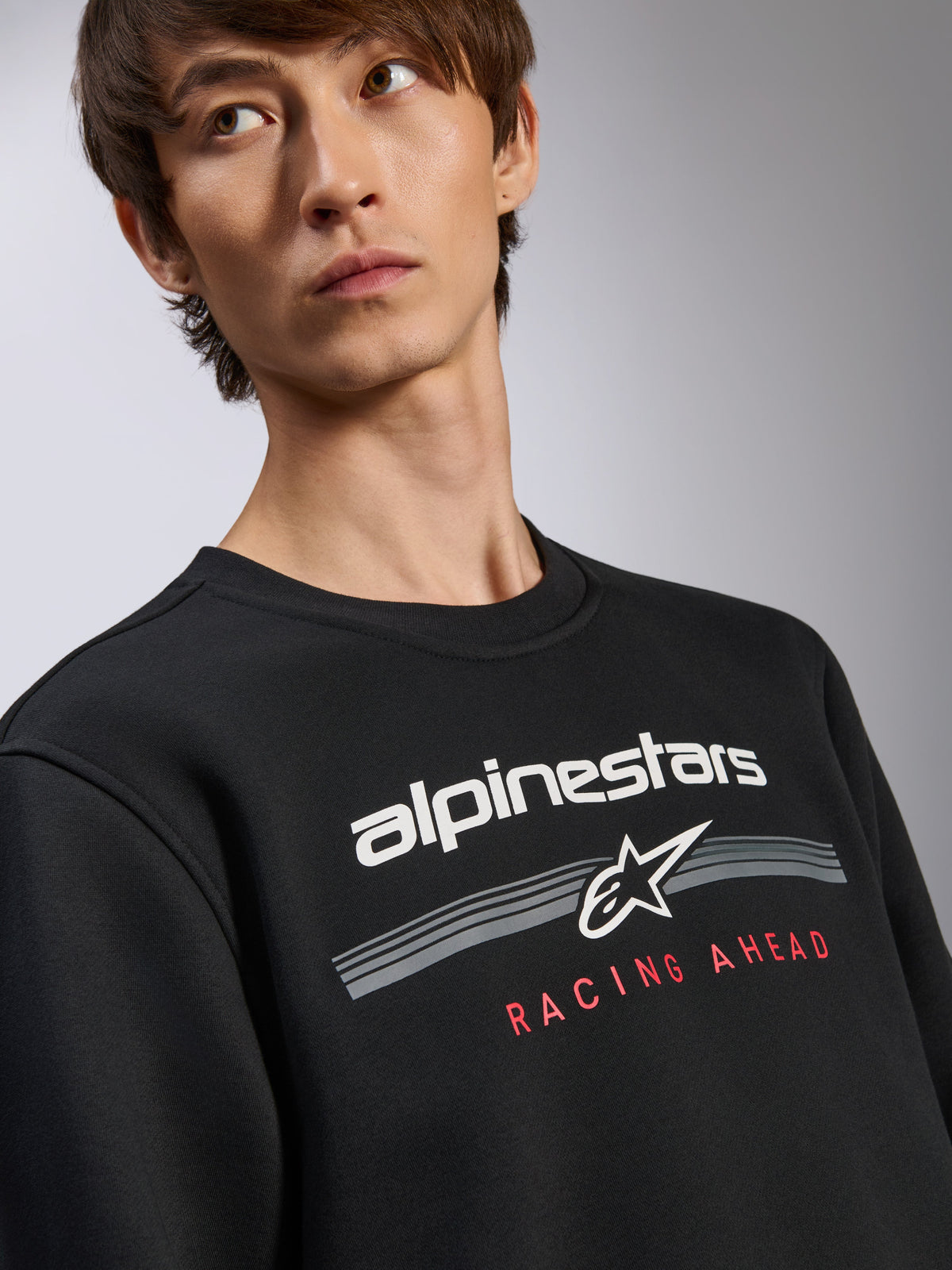 Alpinestars Bettern Crew, camisola preta, logótipo Alpinestars branco com texto 'Racing Ahead' em vermelho, gola redonda, streetwear casual inspirado no desporto motorizado