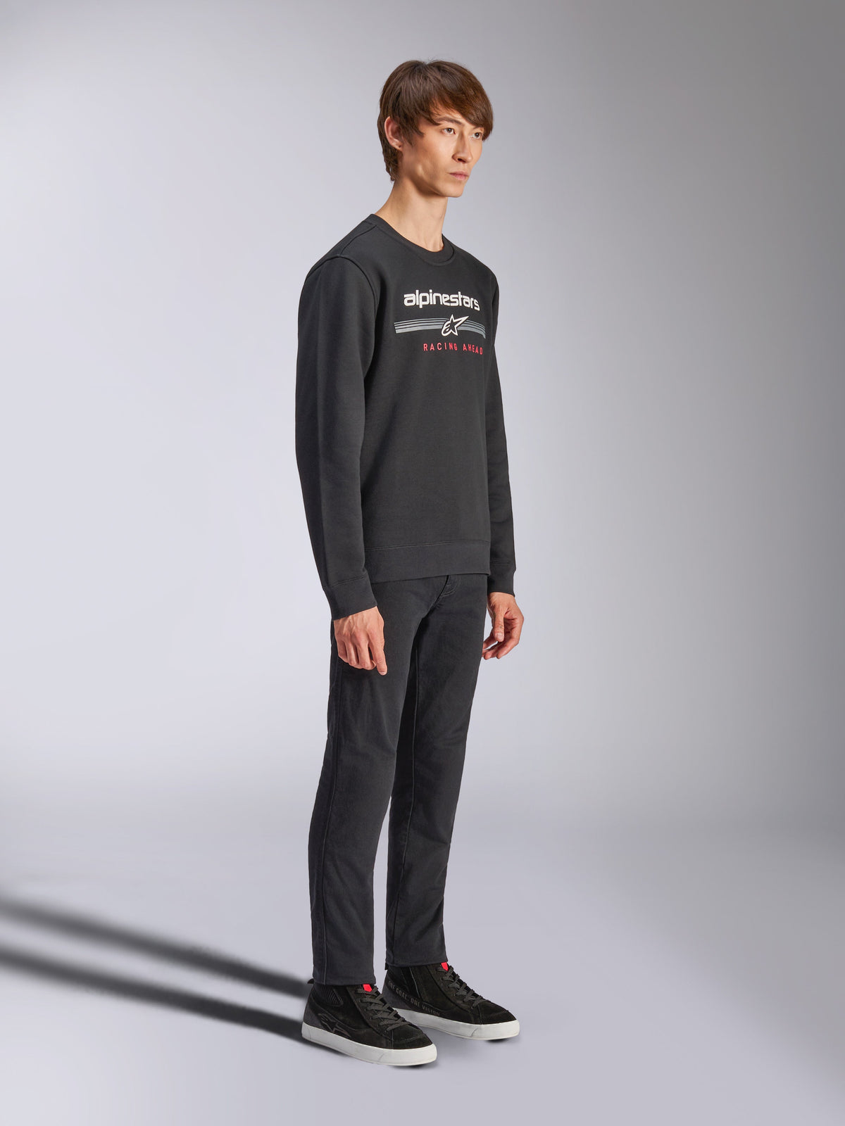 Sweatshirt Alpinestars Bettern Crew, pullover preto de gola redonda, logótipo Alpinestars branco com 'RACING AHEAD' a vermelho no peito, combinado com calças pretas e ténis, streetwear casual inspirado no desporto motorizado