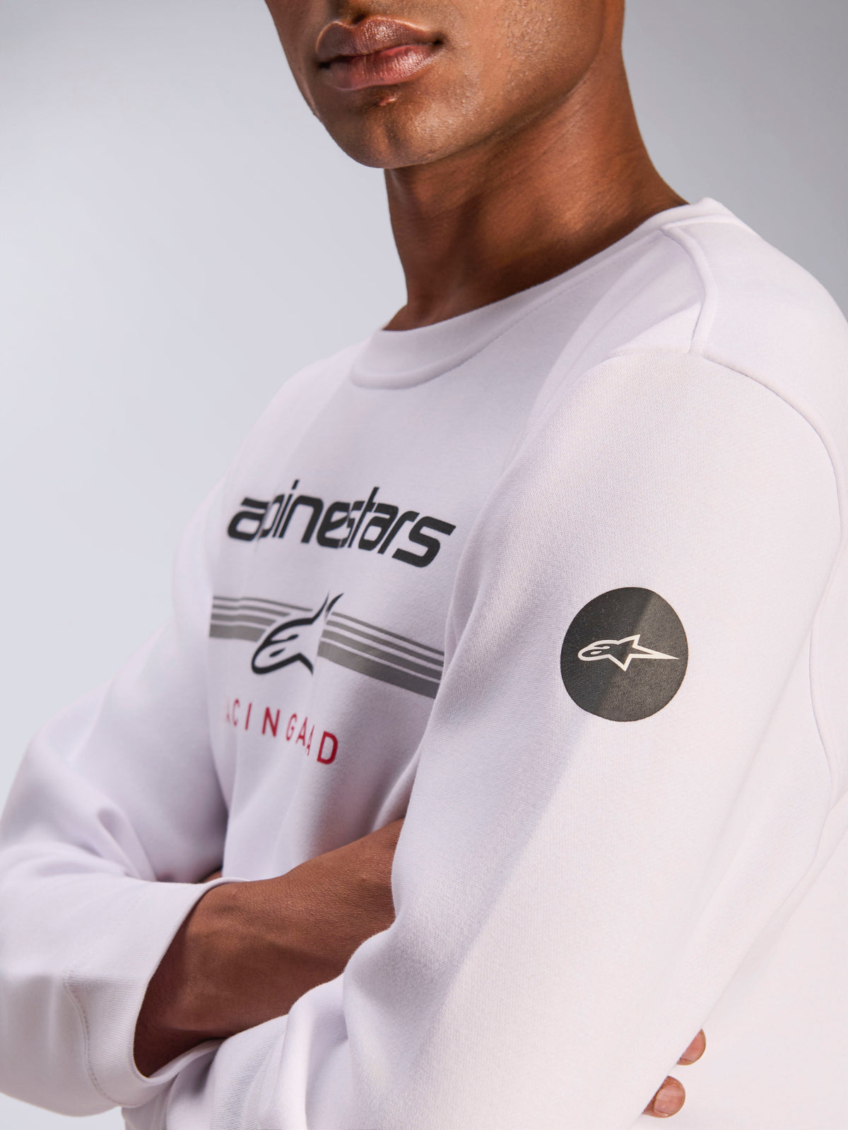Alpinestars Bettern Crew, sweatshirt branca de gola redonda, streetwear casual de motorsport, com gráfico frontal no peito apresentando a marca Alpinestars e listas cinzentas, emblema circular preto com logótipo de estrela na manga, design de pullover em lã polar