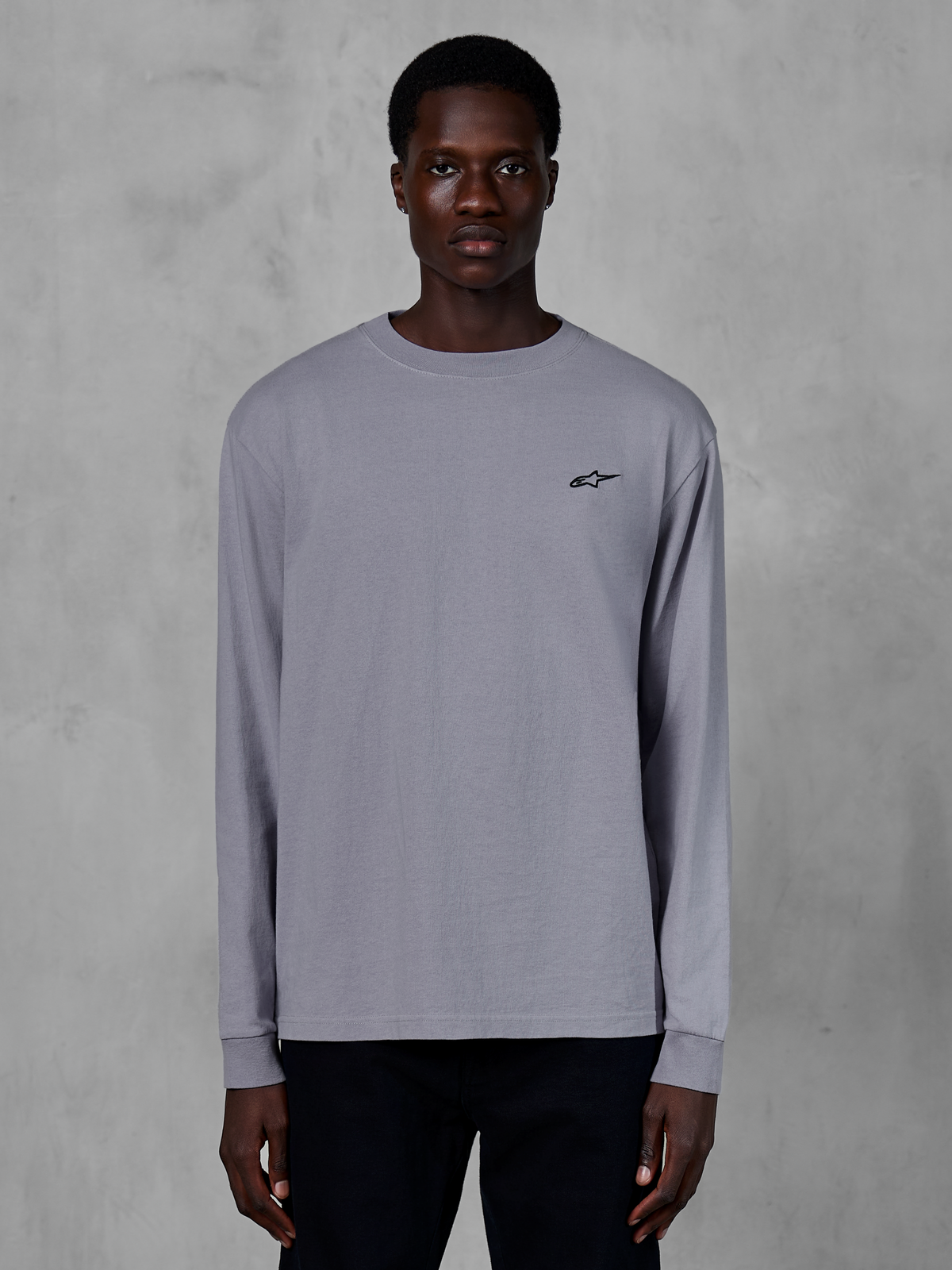 Alpinestars Essentials Ageless LS Tee, t-shirt de manga comprida, prateada, vestida por um modelo, com um pequeno logótipo preto da Alpinestars no peito, corte contemporâneo relaxado, streetwear casual de algodão orgânico