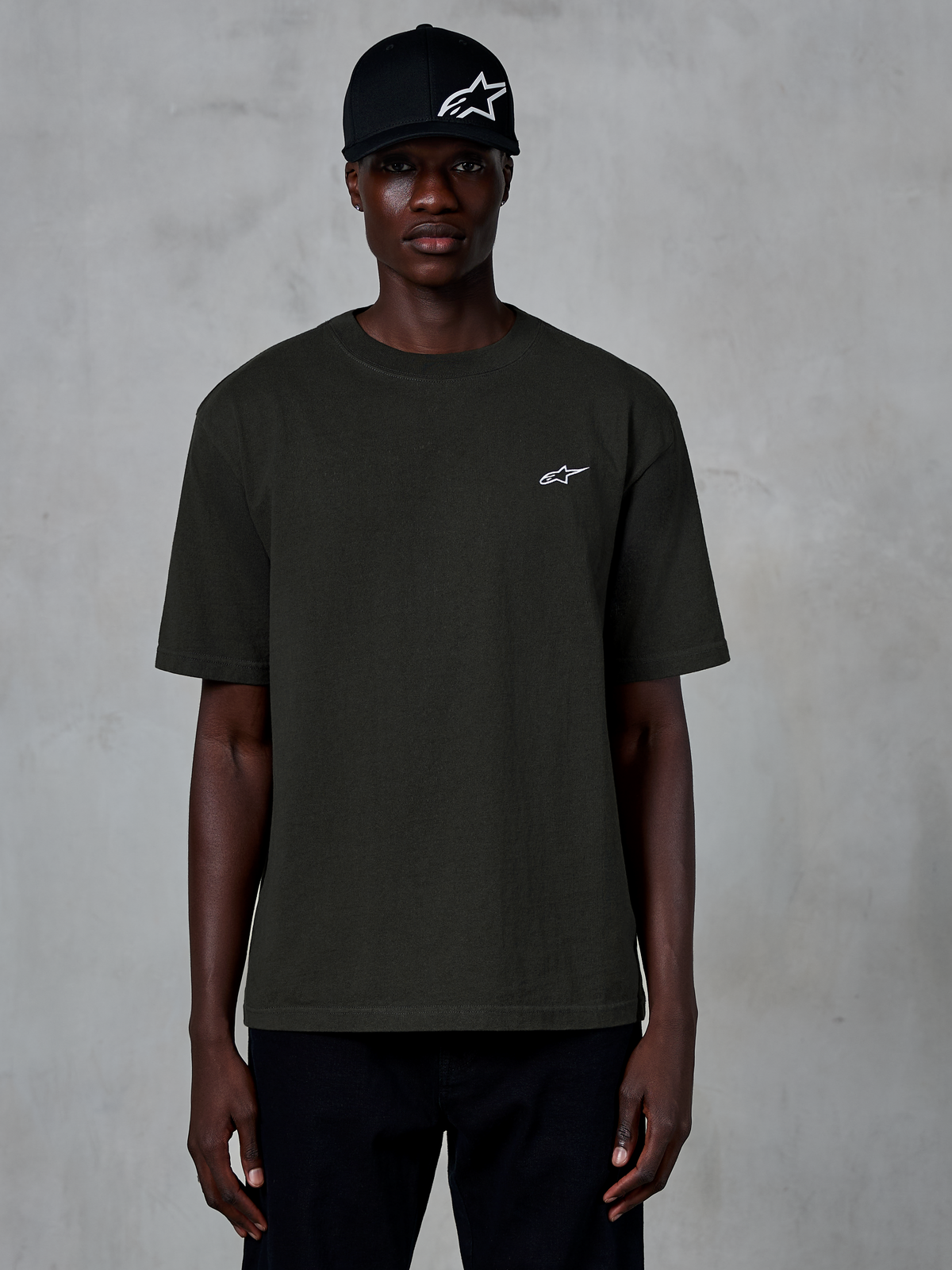 T-shirt Alpinestars Essentials Ageless SS, t-shirt de manga curta, Off Black, usada por um modelo com um boné preto com logótipo, pequeno logótipo Alpinestars branco no peito, streetwear casual inspirado no desporto motorizado