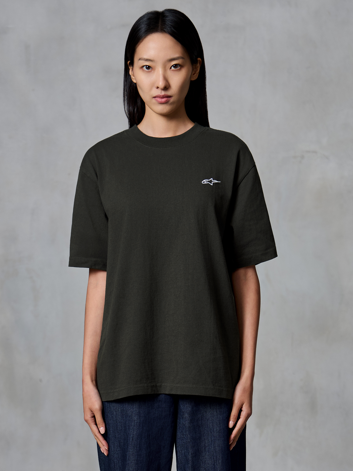 Alpinestars Essentials Ageless SS Tee, t-shirt de manga curta, Off Black, usada por uma modelo feminina, corte relaxado com um pequeno logótipo branco da Alpinestars no lado esquerdo do peito, vestuário casual lifestyle