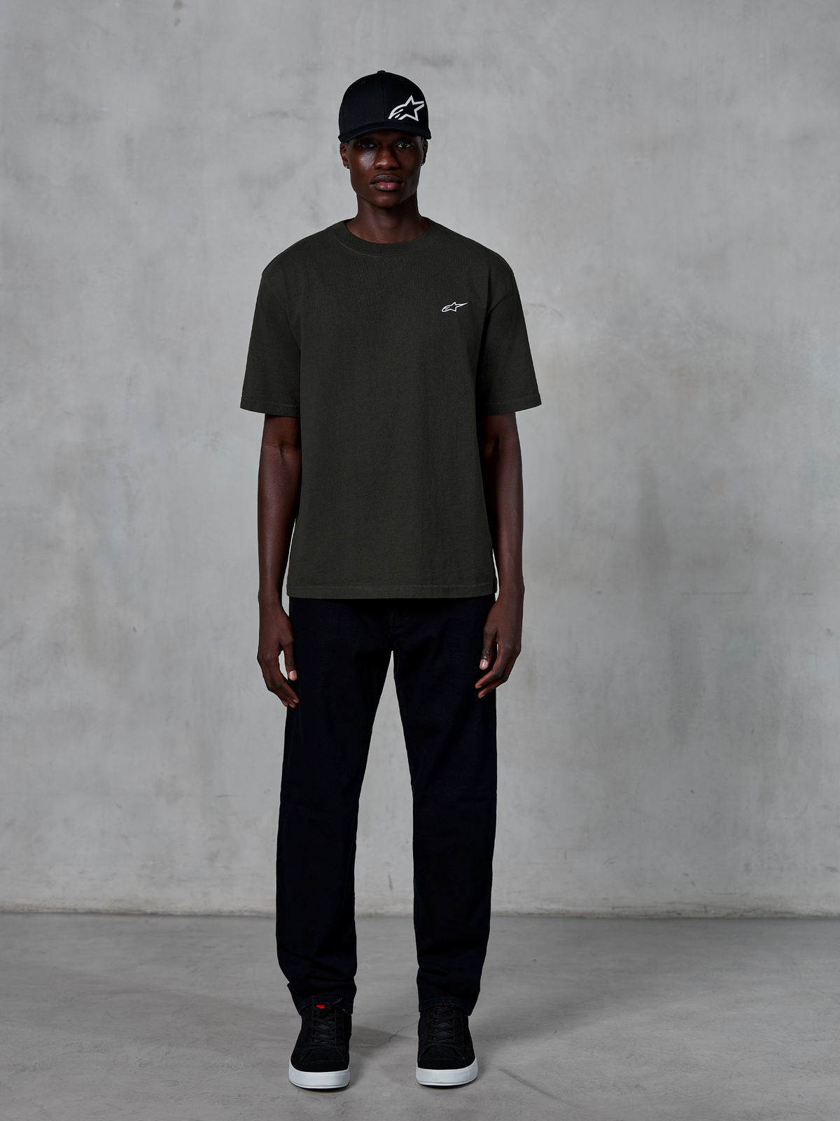 Alpinestars Essentials Ageless SS Tee, t-shirt de manga curta, Off Black, com um pequeno logótipo Alpinestars branco no peito, usada por um modelo com boné e calças pretas para um look lifestyle clean