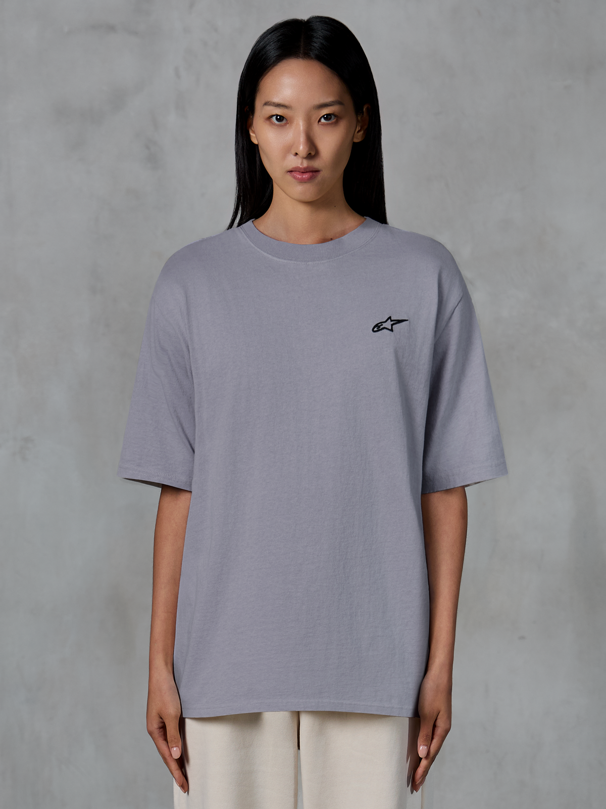 Alpinestars Essentials Ageless SS Tee, t-shirt de manga curta, prateada, com um pequeno logótipo Alpinestars preto no peito, corte relaxado e contemporâneo, algodão orgânico, streetwear casual usada por uma modelo