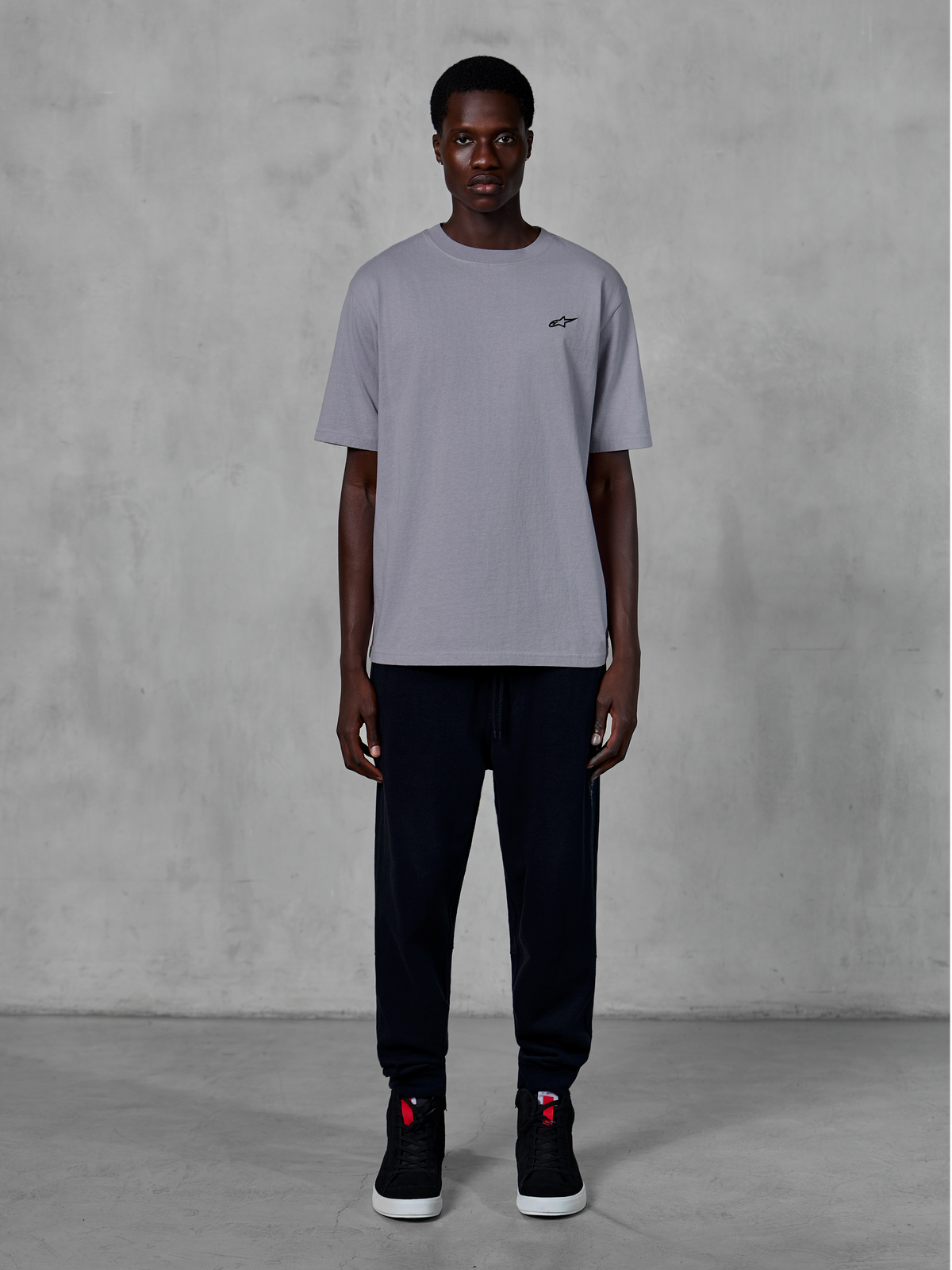 Alpinestars Essentials Ageless SS Tee, t-shirt de manga curta, prateada, com um pequeno logótipo preto no peito, combinada com calças joggers pretas e sapatilhas, streetwear casual de desportos motorizados
