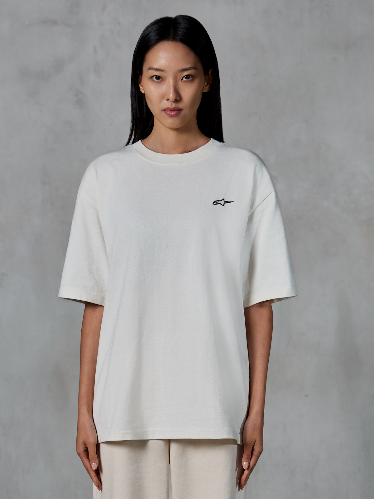 Alpinestars Essentials Ageless SS Tee, t-shirt de manga curta, Off White, vestida por modelo feminina, com um pequeno logótipo Alpinestars preto no peito, ajuste relaxado, streetwear casual lifestyle