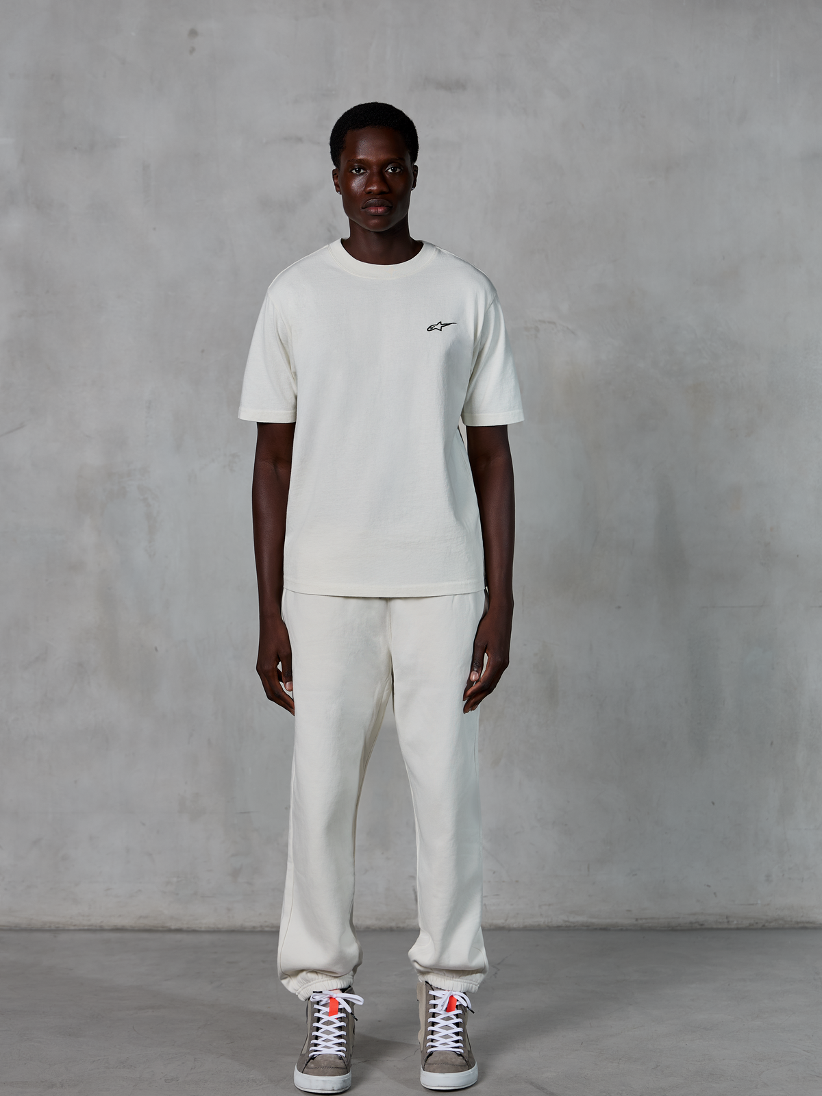 Alpinestars Essentials Ageless SS Tee, t-shirt de manga curta, Off White, com um pequeno logótipo Alpinestars preto no peito, combinada com calças joggers a condizer e sapatilhas para um visual casual e descontraído