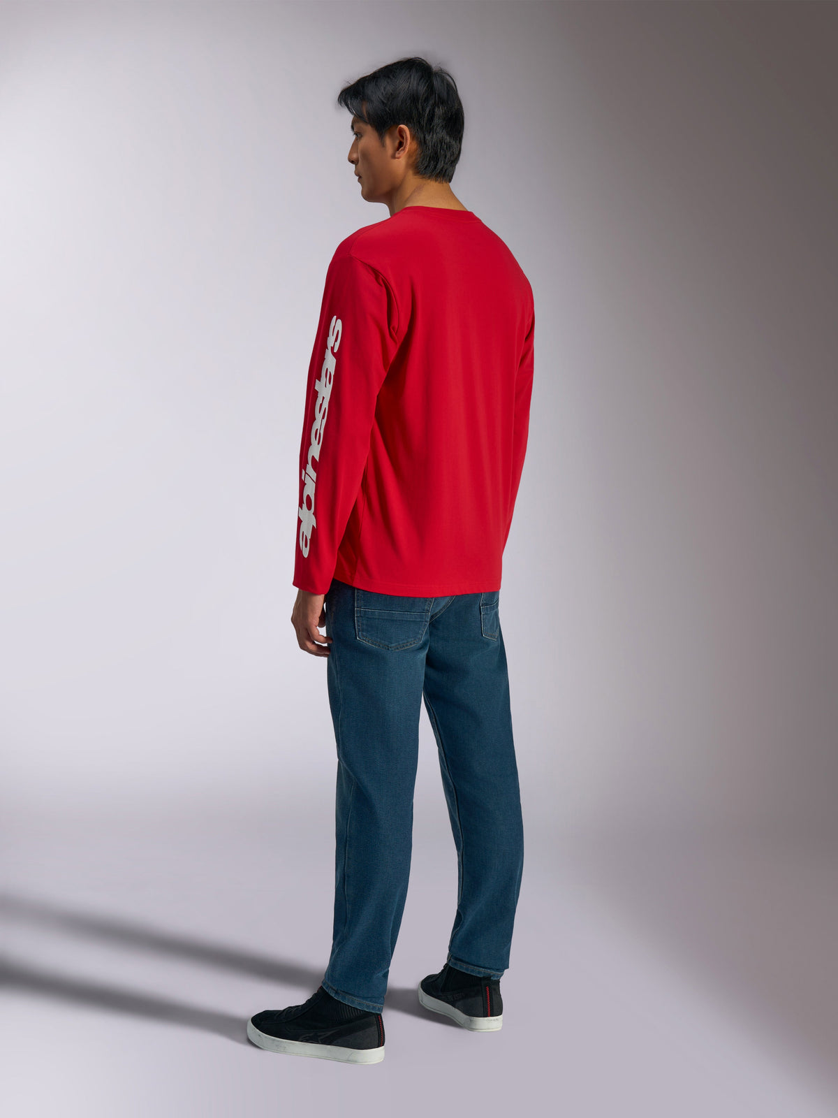 Alpinestars Trackside CSF Tee, Long Sleeve T-Shirt, Red, featuring a white vertical Alpinestars logo on the sleeve, worn by a model with blue jeans and black sneakers, casual motorsport-inspired streetwear