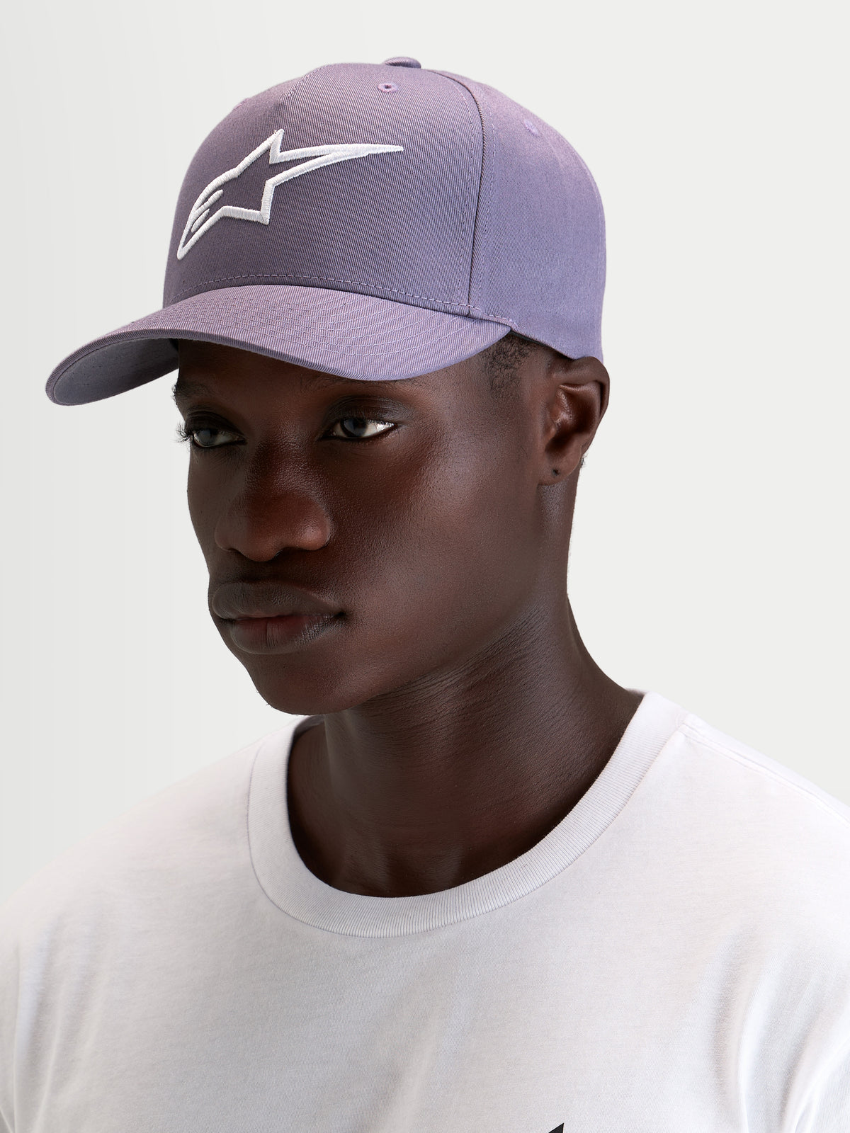 Alpinestars Ageless Snapback Hat, sportswear curved bill cap in dusty purple and white, worn by a model showcasing the structured crown and 3D embroidered Astars logo