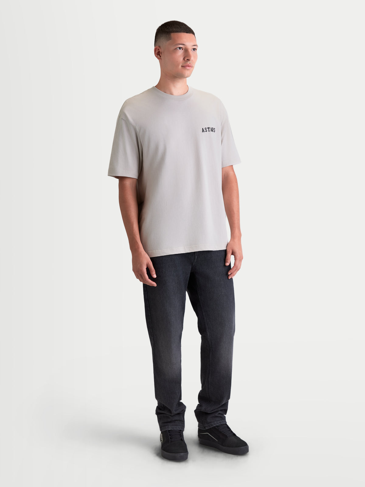 Alpinestars T-Shirt Latitude Oversized CSF, t-shirt de manga curta num modelo, cor cinzento cimento, corte oversized descontraído com logótipo ASTARS preto no peito, sportswear casual em mistura de algodão e poliéster.