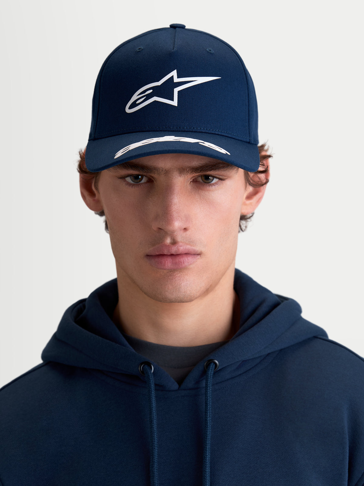 Alpinestars Chapéu Arclight, boné de aba curva para homem, azul-escuro e branco, vista frontal no modelo, com copa estruturada, logótipo Astars em relevo texturizado e sarja de algodão premium.
