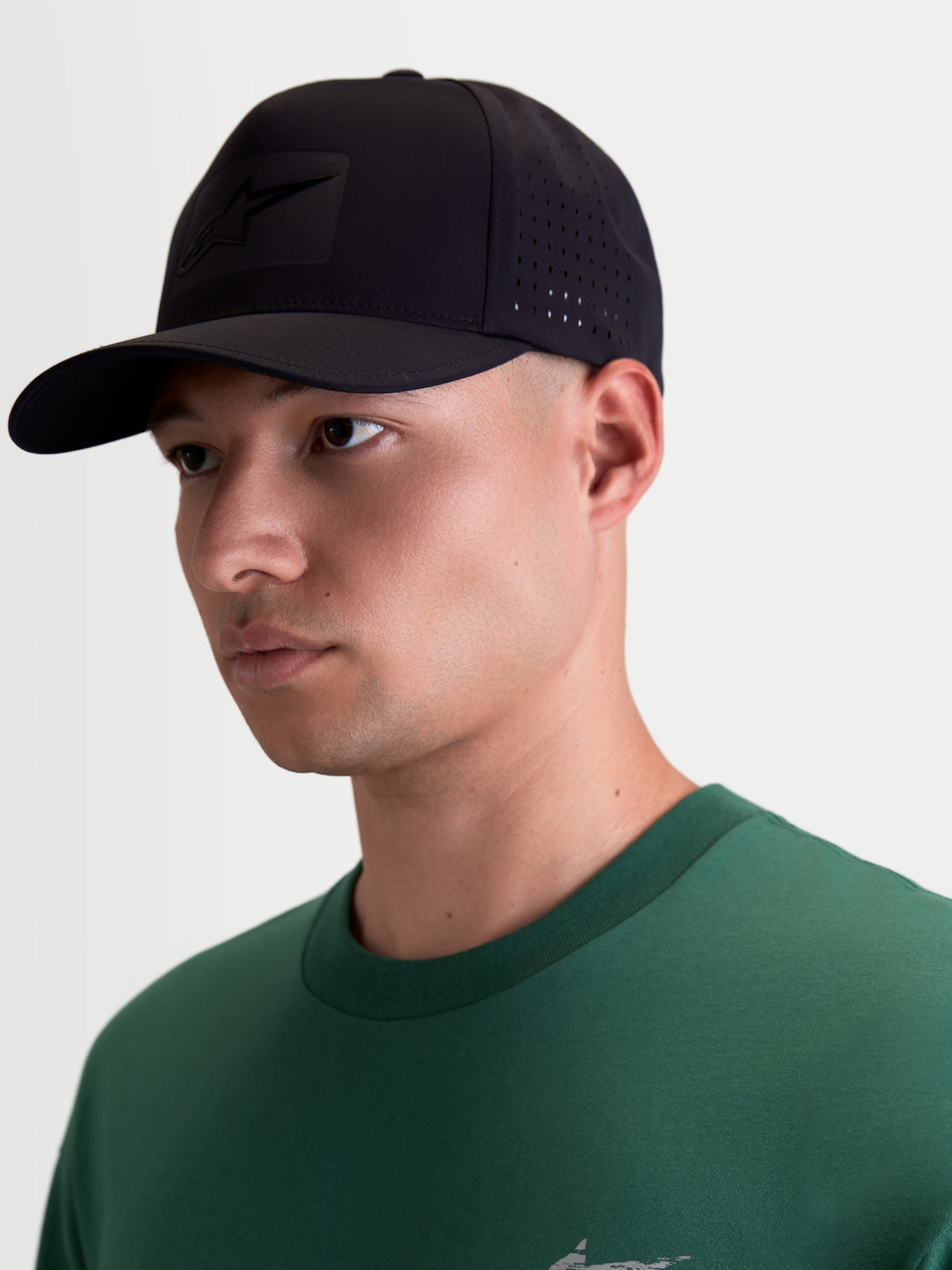 Alpinestars Boné Algo Perf Adjustable, boné de estilo motorsport preto, vista em modelo, aba curva e tecido técnico com perfurações laterais para respirabilidade, logótipo Astars em soldadura sónica tonal.