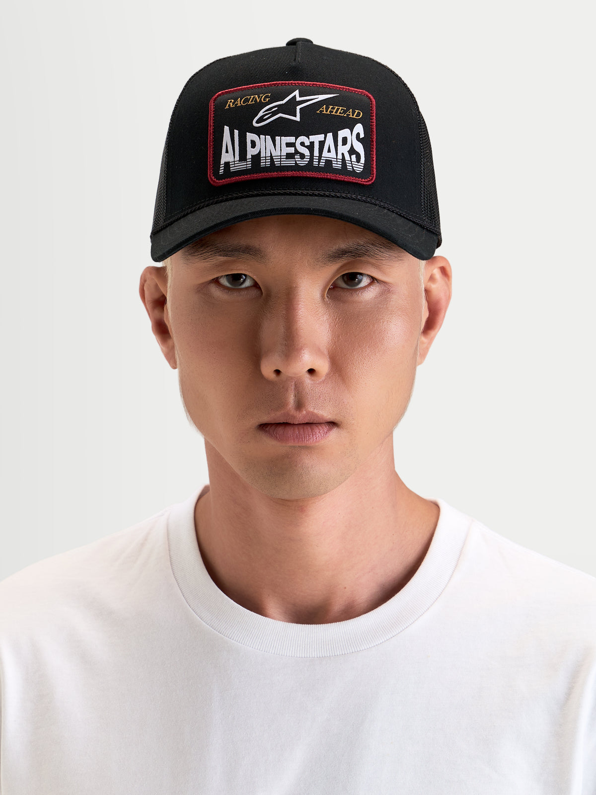 Alpinestars Boné Trucker Hemmings, boné desportivo para homem, preto, vista frontal num modelo a mostrar o logótipo frontal tecido e painéis em malha respirável