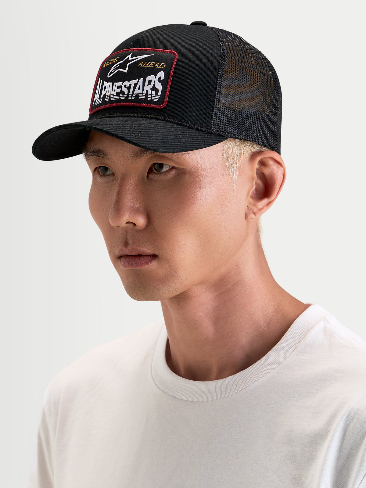 Alpinestars Hemmings Trucker Hat, sportswear snapback cap worn by a model, black with breathable poly mesh back panels and a front Alpinestars woven logo patch
