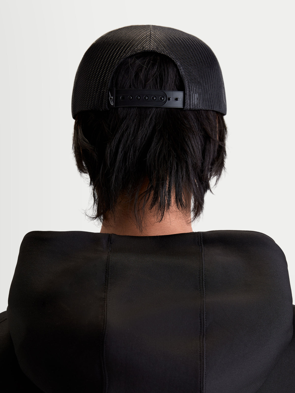 Alpinestars Boné Trucker Gravel, boné unissexo preto, vista traseira em modelo mostrando a malha respirável e o fecho snapback ajustável, sportswear casual.