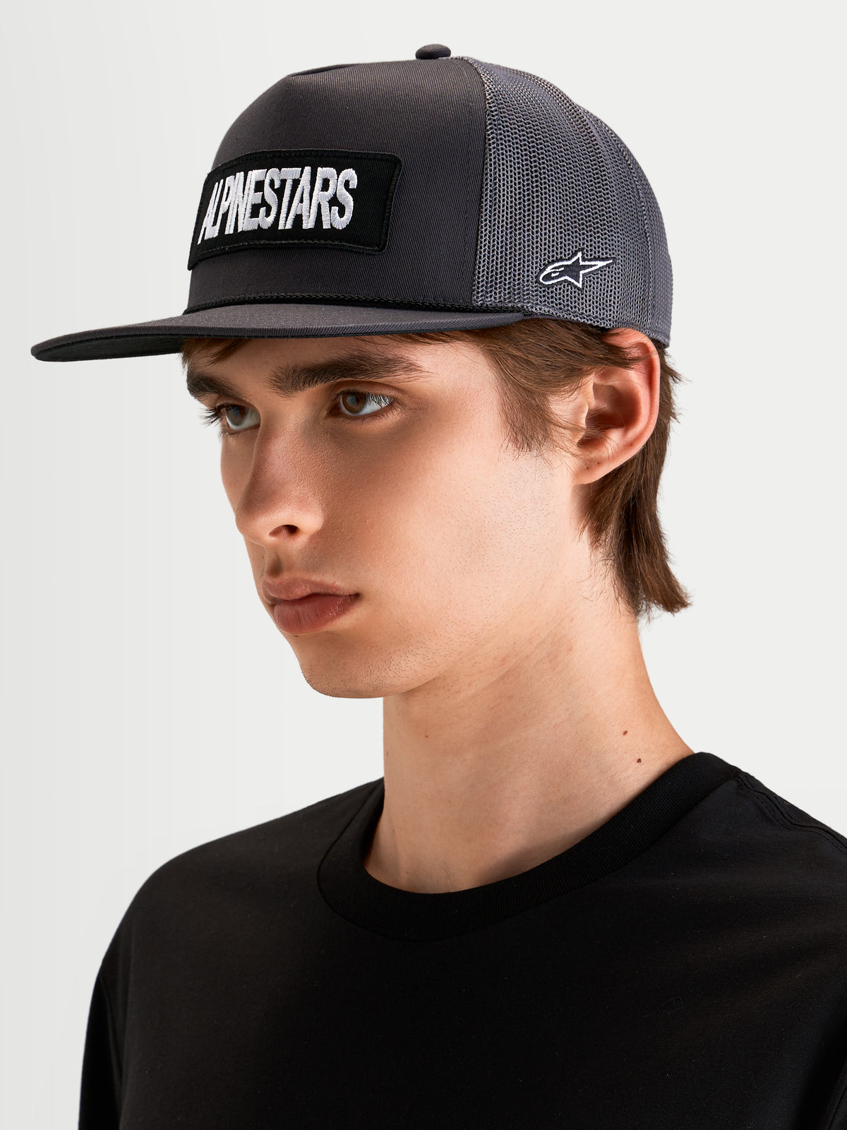 Alpinestars Boné Trucker Ten, boné sportswear de pala plana cinzento, usado por um modelo, com patch frontal bordado do logótipo Alpinestars e bordado do logótipo Astars lateral