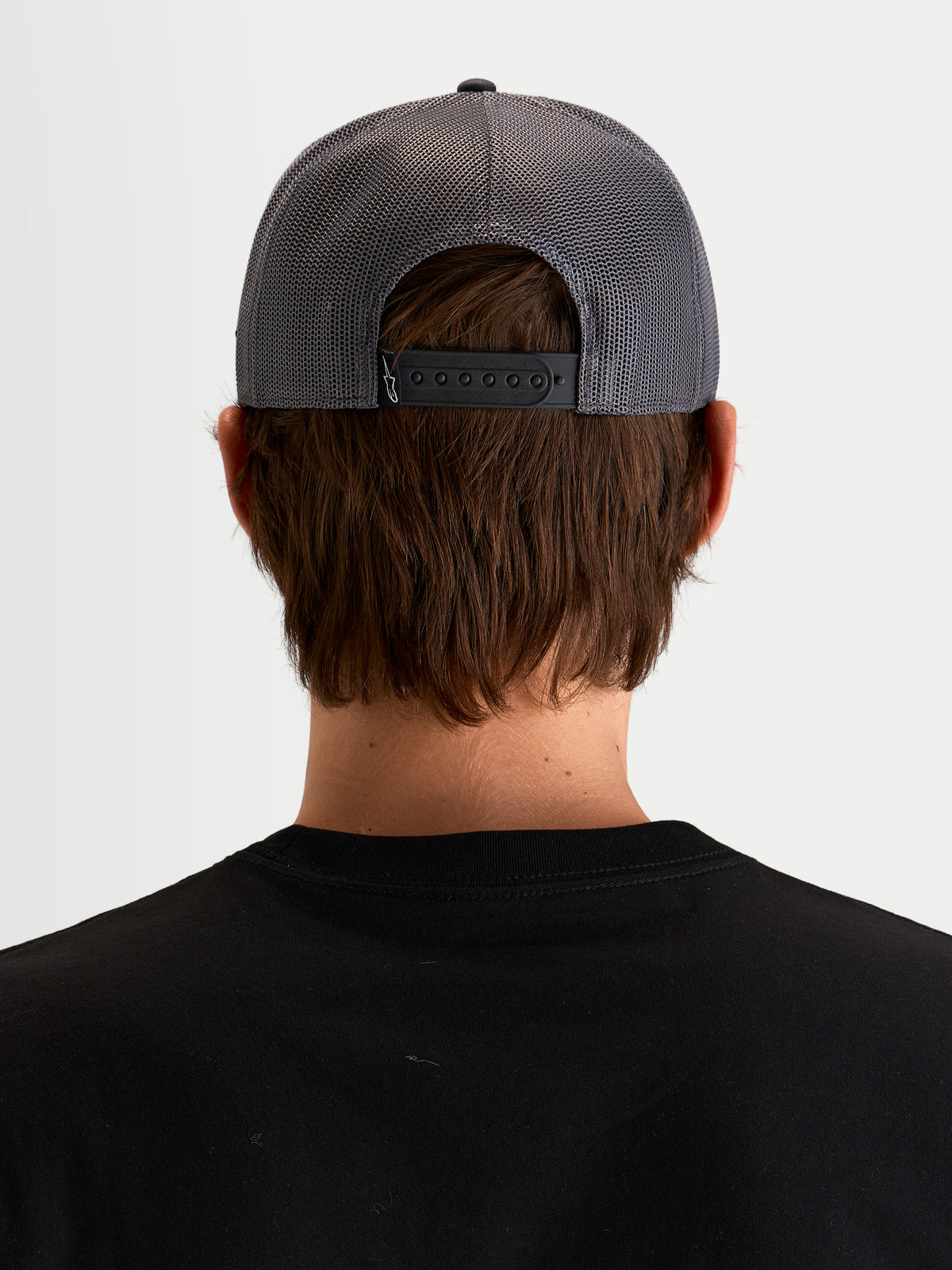 Alpinestars Boné Trucker Ten, boné desportivo snapback em cinzento escuro, vista traseira num modelo a mostrar o fecho snapback ajustável, painéis traseiros em rede e detalhe de etiquetagem traseira