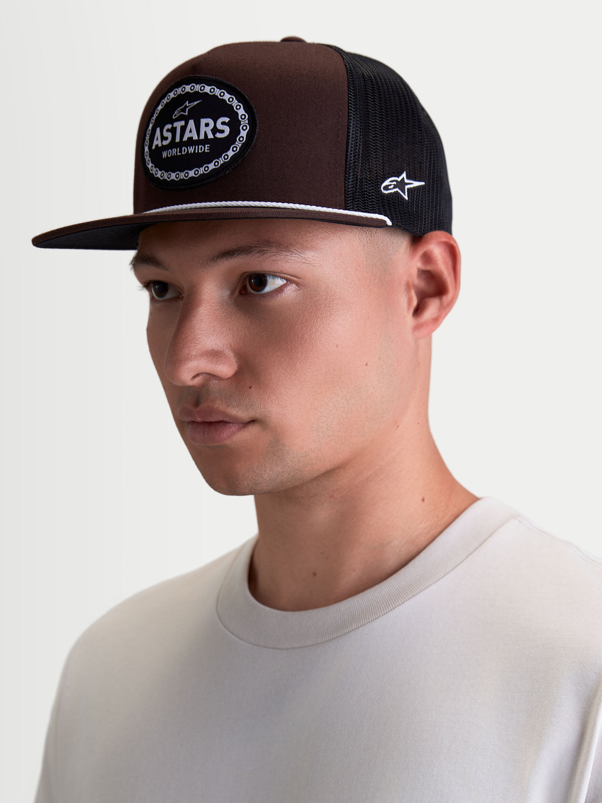 Alpinestars Boné Trucker Hotlink, boné de sportswear em modelo, castanho e preto, com aba plana e copa estruturada em sarja, patch frontal com logótipo Astars e rebordo em corrente de bicicleta.