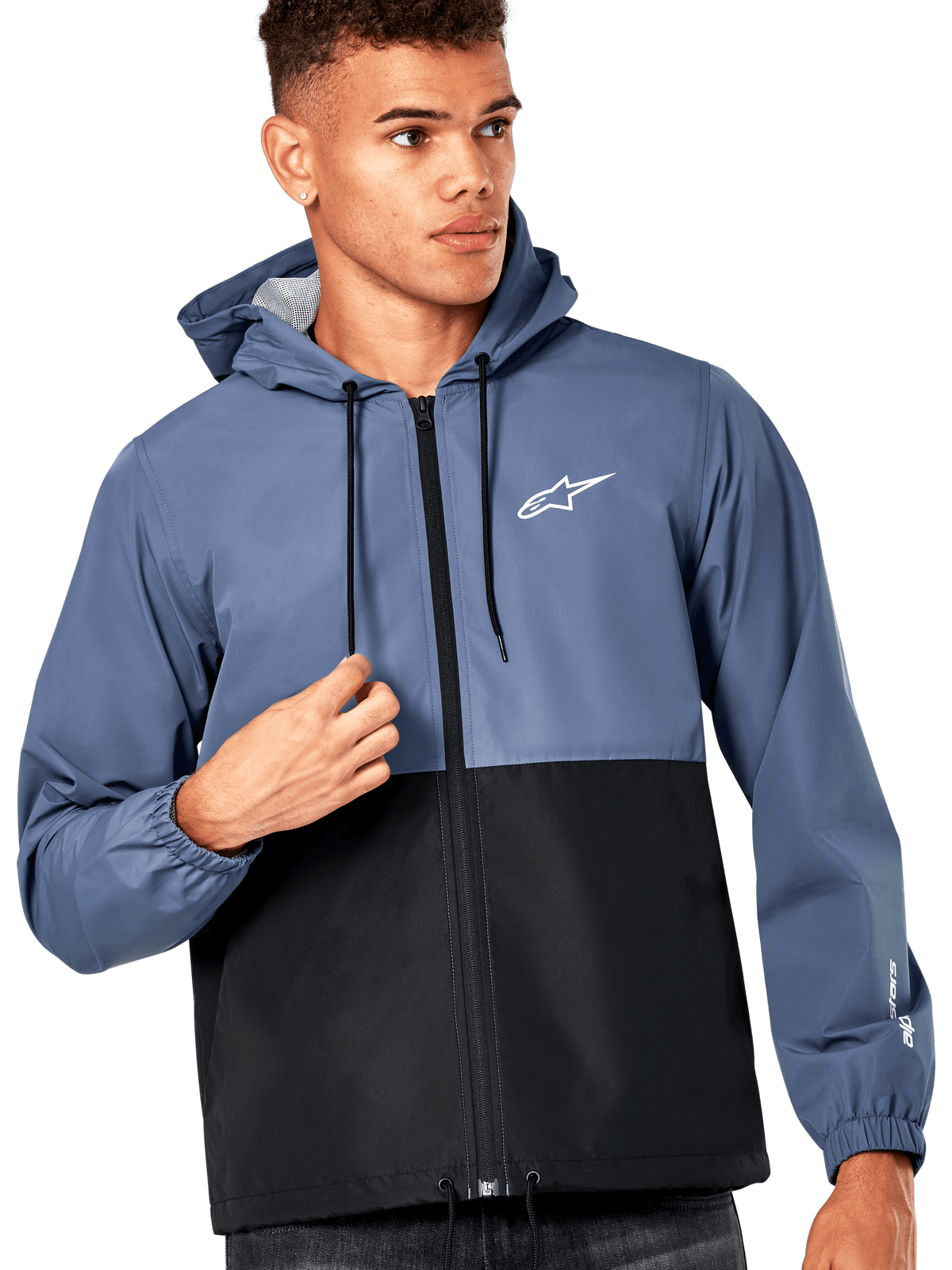 Modelo masculino a usar o Casaco Corta-Vento Speeder da Alpinestars, design em blocos de cor azul ardósia e preto, com capuz e cordões pretos, logótipo branco no peito, corta-vento casual inspirado no desporto motorizado