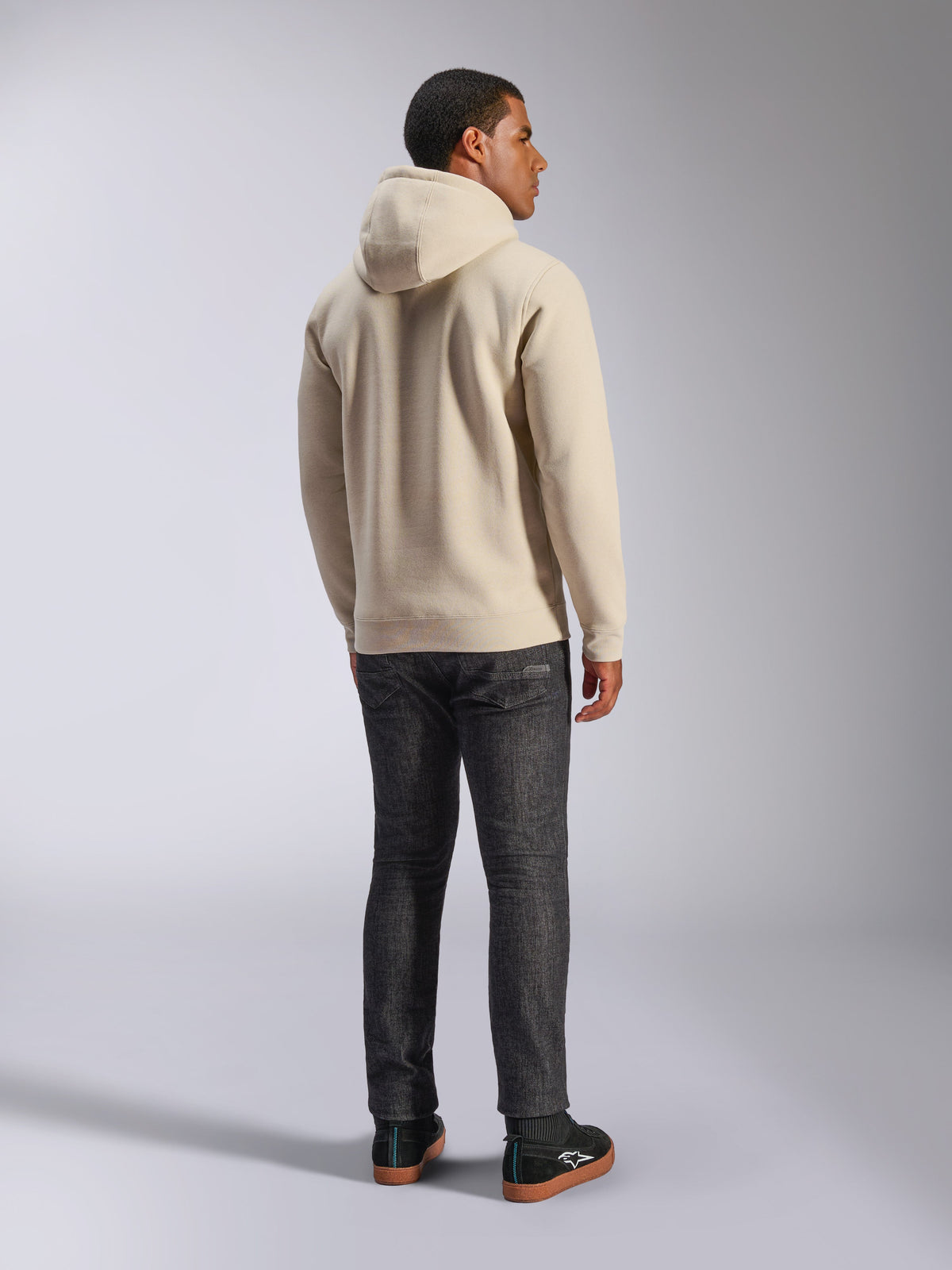 Alpinestars Ageless V3 Hoodie, casual off-white hooded pullover fleece shown from the back, features ribbed cuffs and hem, worn with dark slim-fit jeans and black Alpinestars sneakers