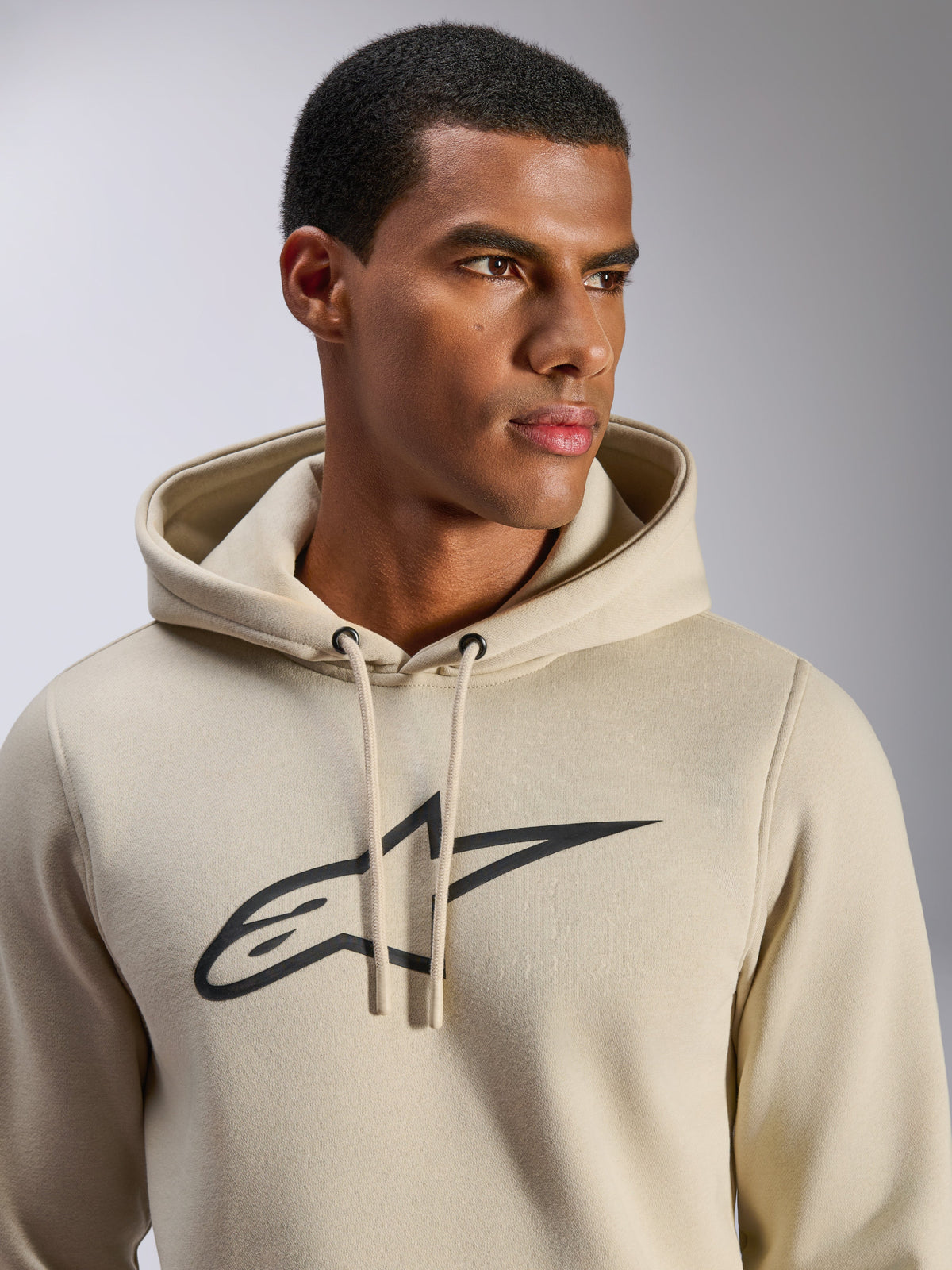 Alpinestars Ageless V3 Hoodie, casual sportswear, off-white with black embroidered Alpinestars star logo, drawstring hood, close-up view on model, soft fleece, modern motorsport-inspired design