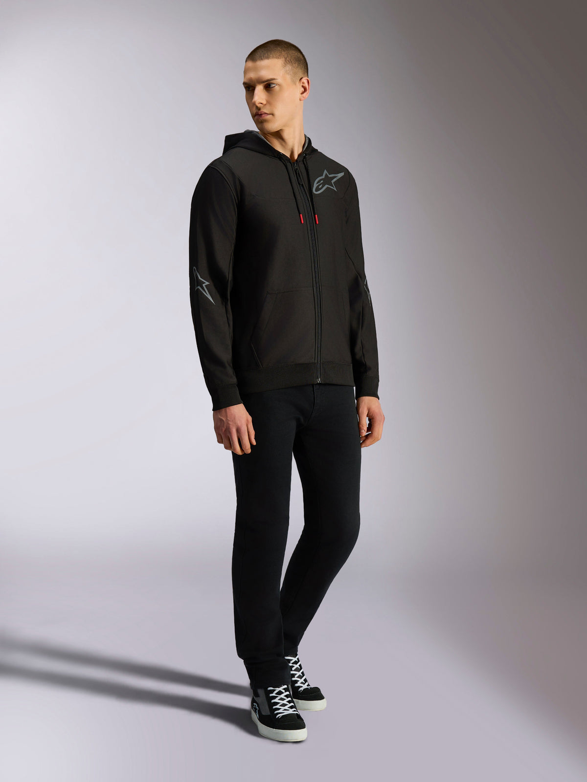 Alpinestars Sessions V3 Hoodie, camisola em fleece de poliéster com fecho frontal, preto e cinzento, logótipos cinzentos no peito e na manga, capuz com cordões com pontas vermelhas, vista de corpo inteiro de modelo em estilo urbano casual de desportos motorizados
